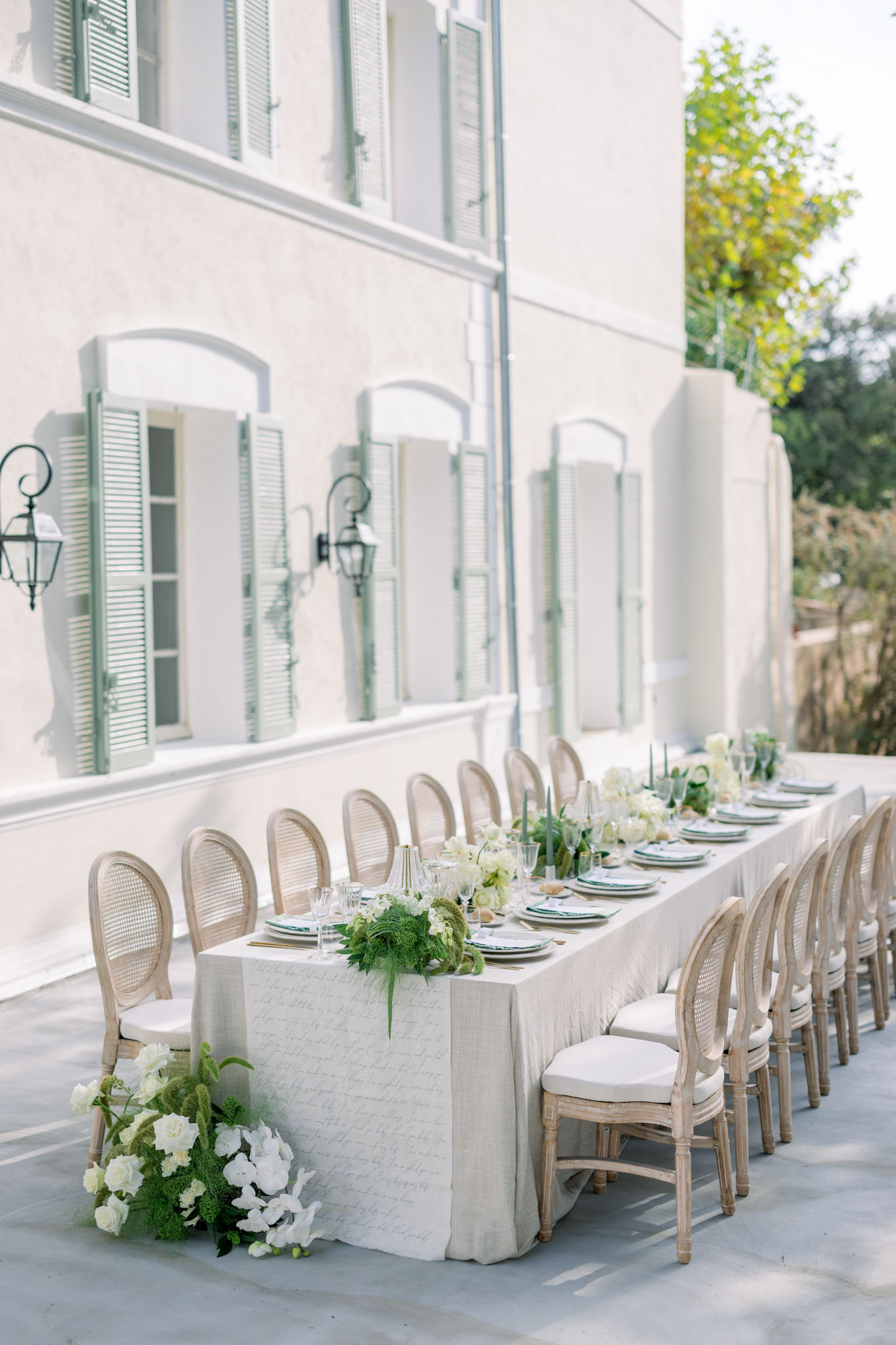 Long outdoor reception table with ivory linen, navy chargers, rattan chairs and white hydrangea centerpieces