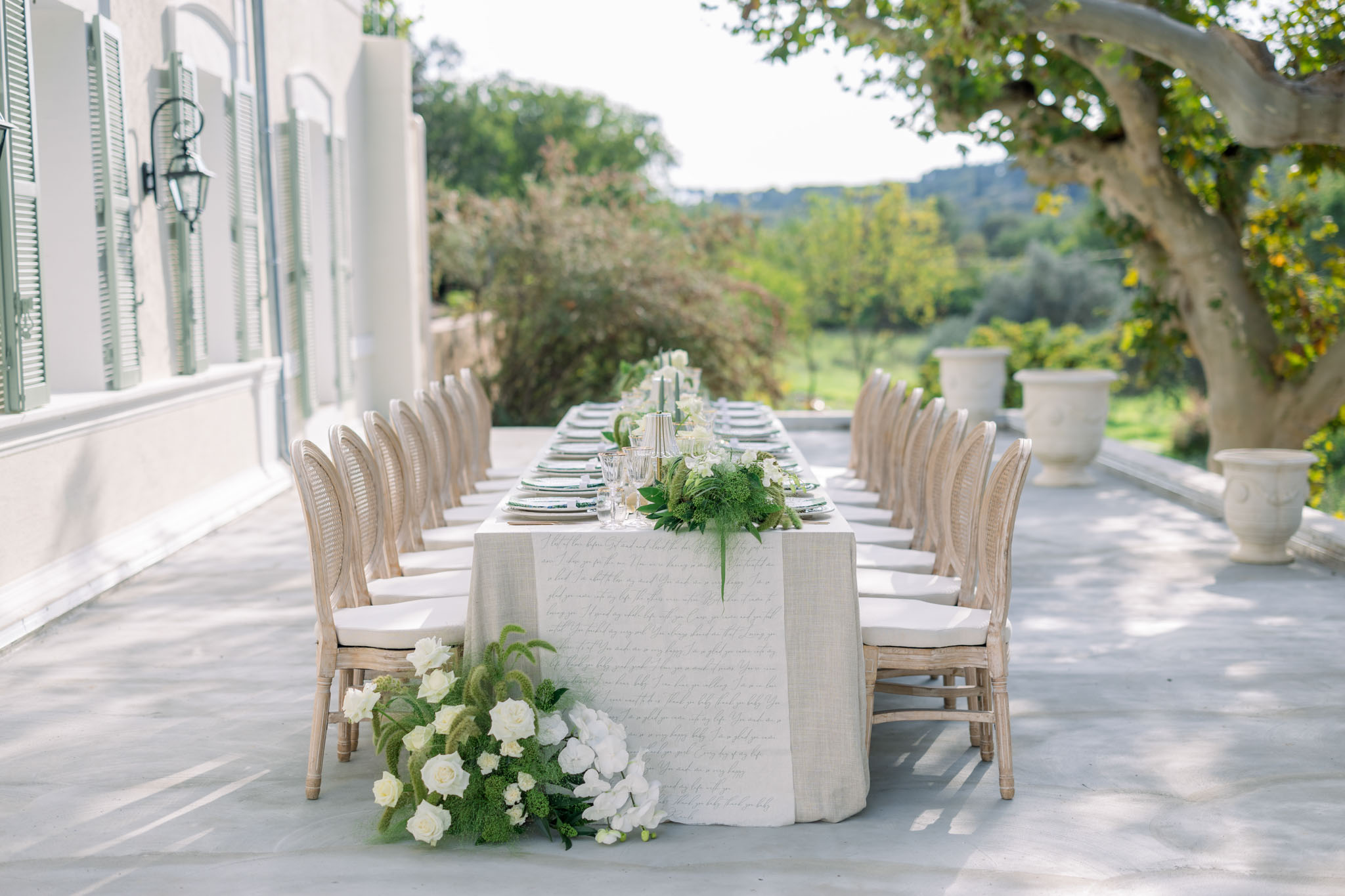 Long reception table with white roses and hydrangeas on a stone terrace overlooking rolling hills