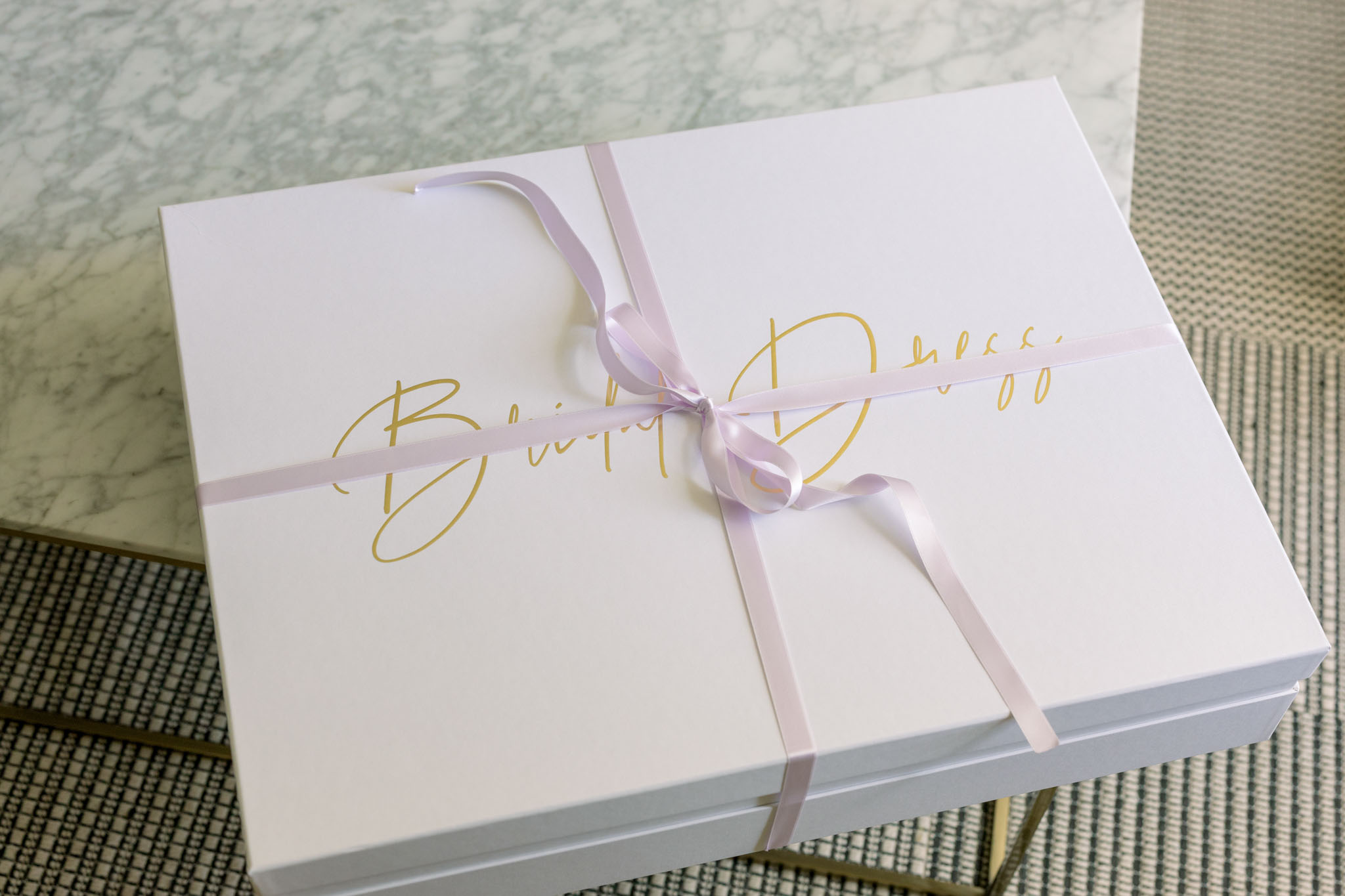 White stationery box tied with pale lavender silk ribbon and gold calligraphy on marble surface