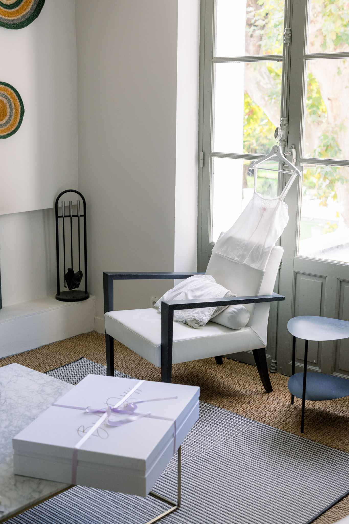 Wedding dress hanging on acrylic hanger by tall window with sage-green frames