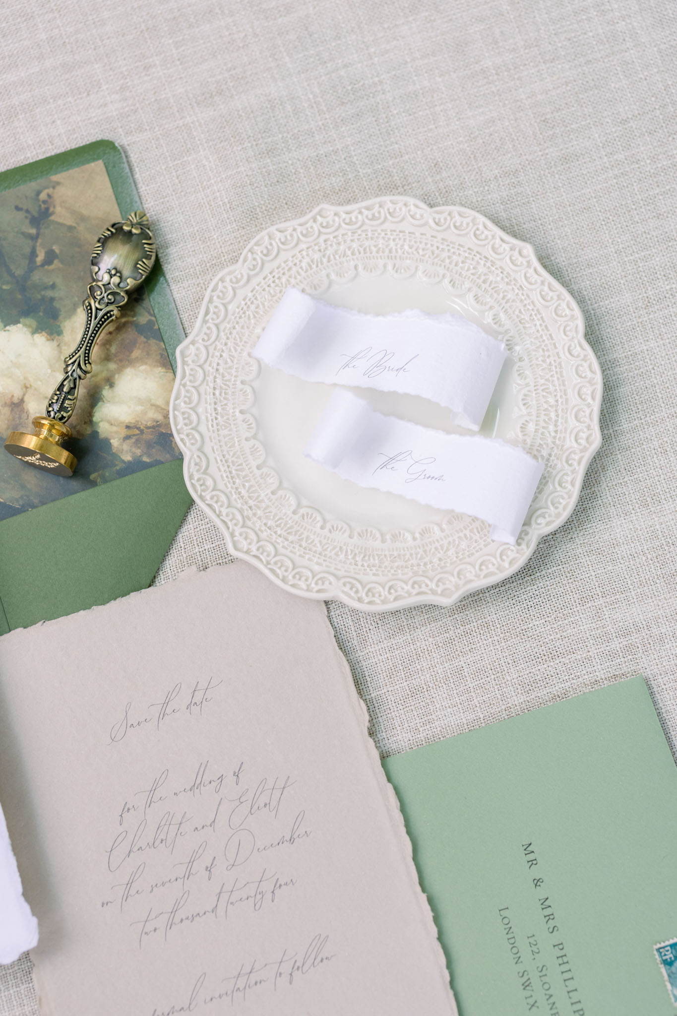 Flat lay of wedding stationery with cream plate, handwritten place cards, sage green envelope, and antique silver spoon