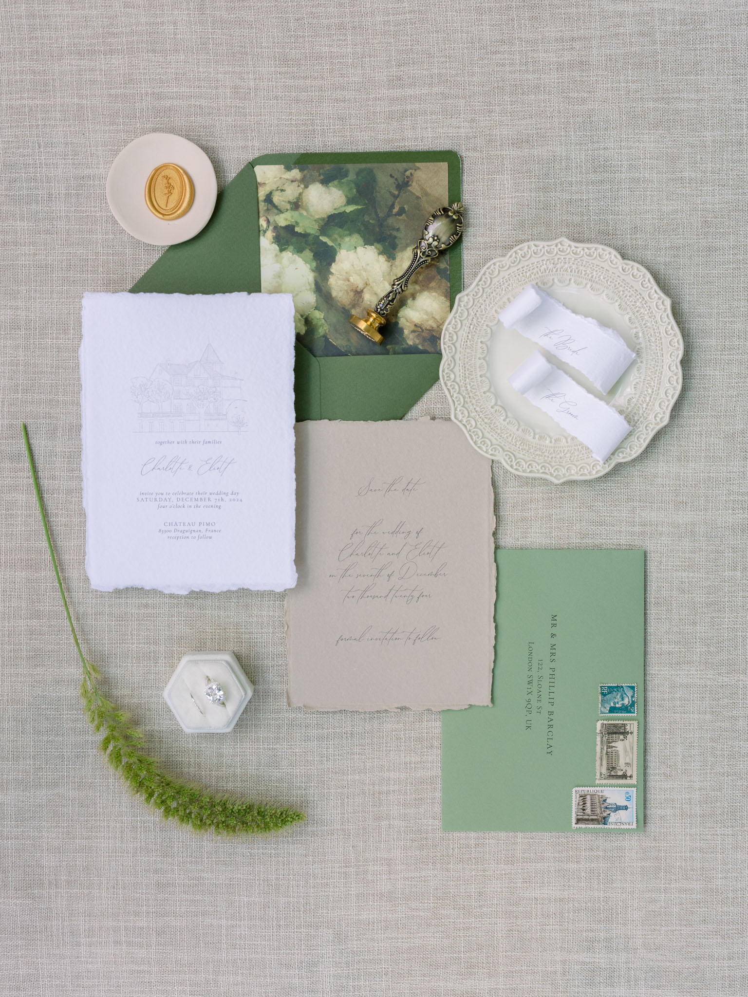 Flat lay of wedding stationery with sage envelope, vintage stamps, and botanical photograph