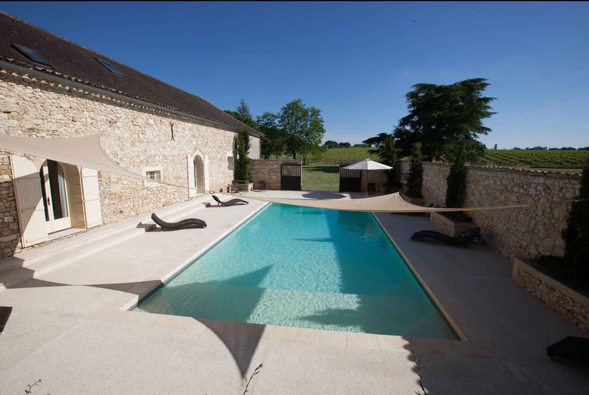 Rectangular pool with turquoise water surrounded by limestone terrace and sun loungers at a French vineyard estate