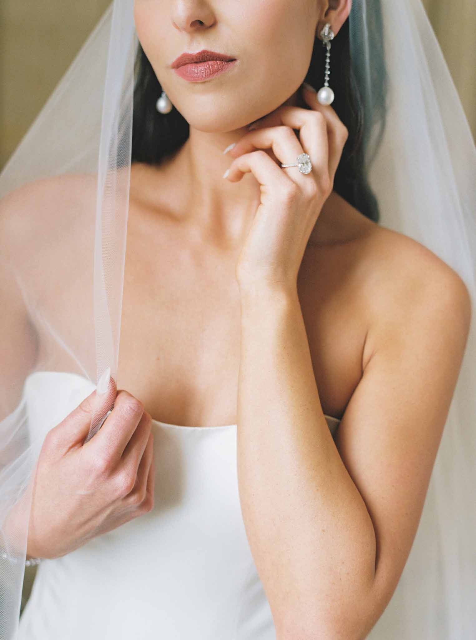 Close-up portrait of bride in strapless white dress with pearl drop earrings and diamond engagement ring near her face