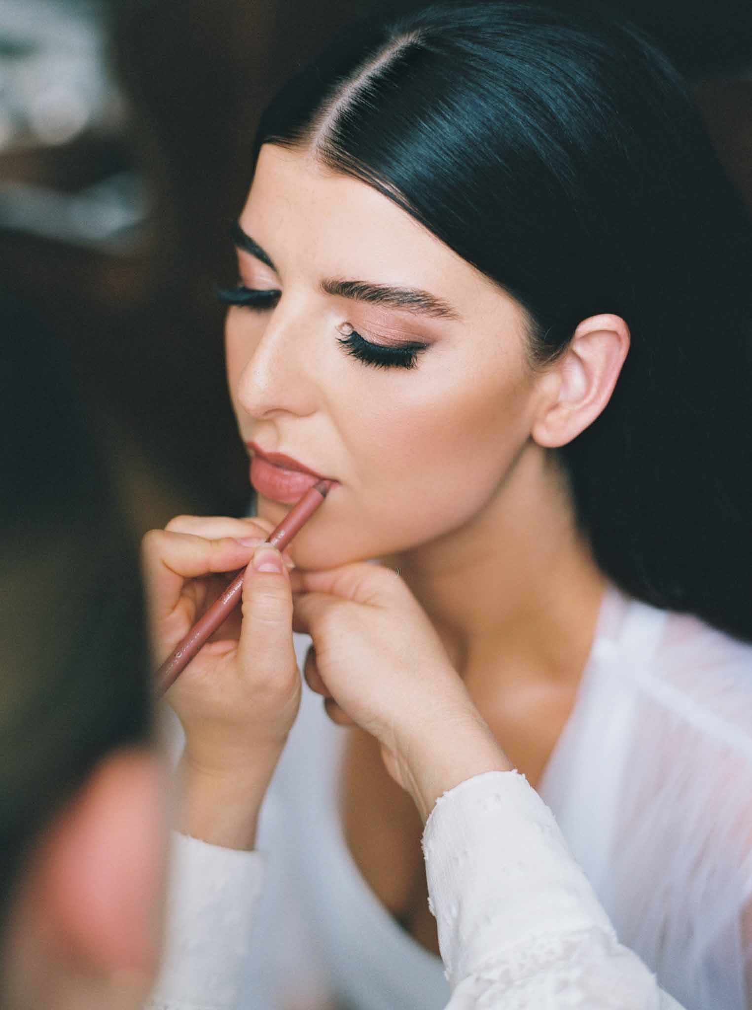 Makeup artist applies lip color to bride in profile during getting ready preparations