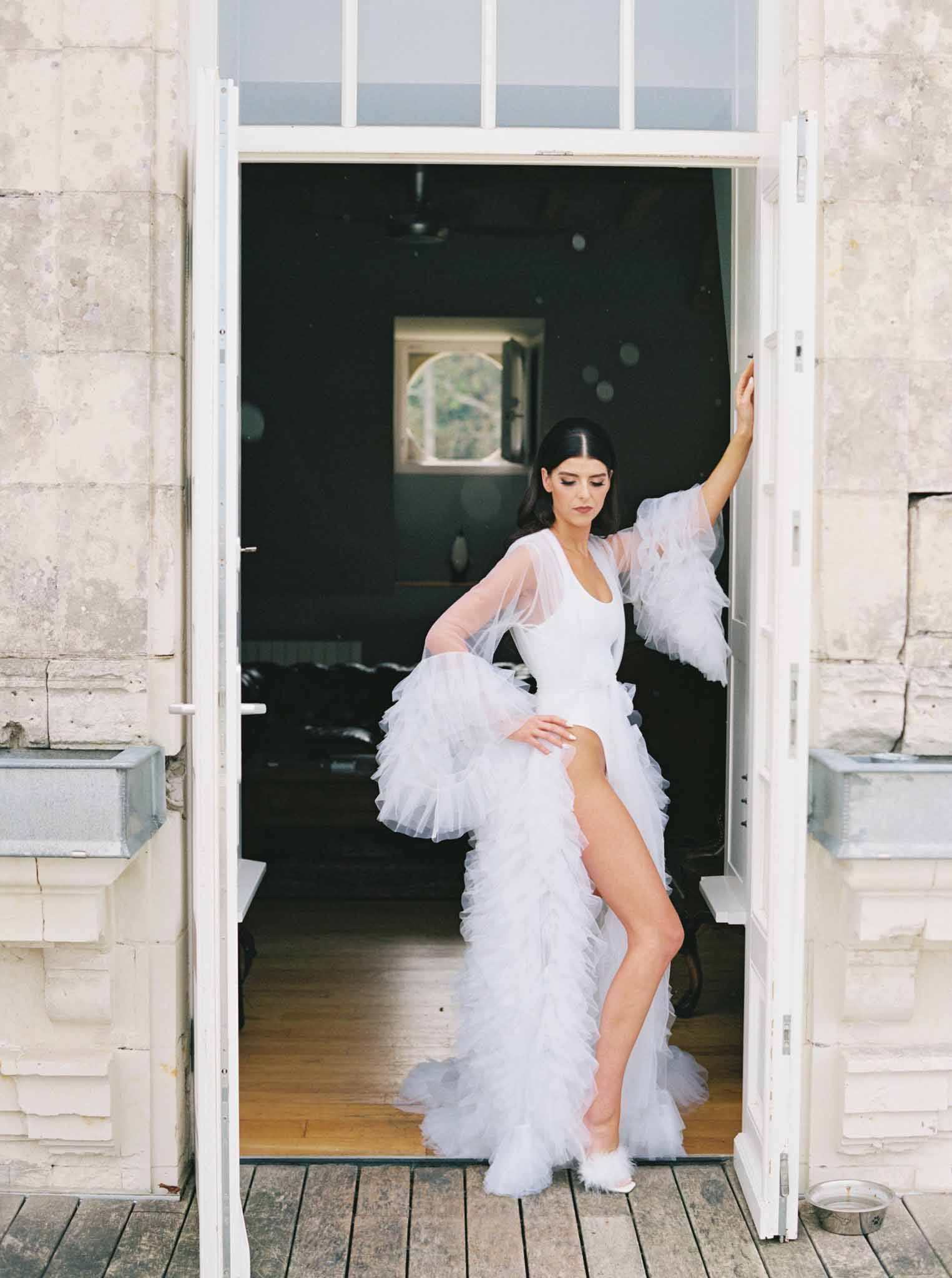 Bride in white tulle robe posing in doorway during getting-ready preparations