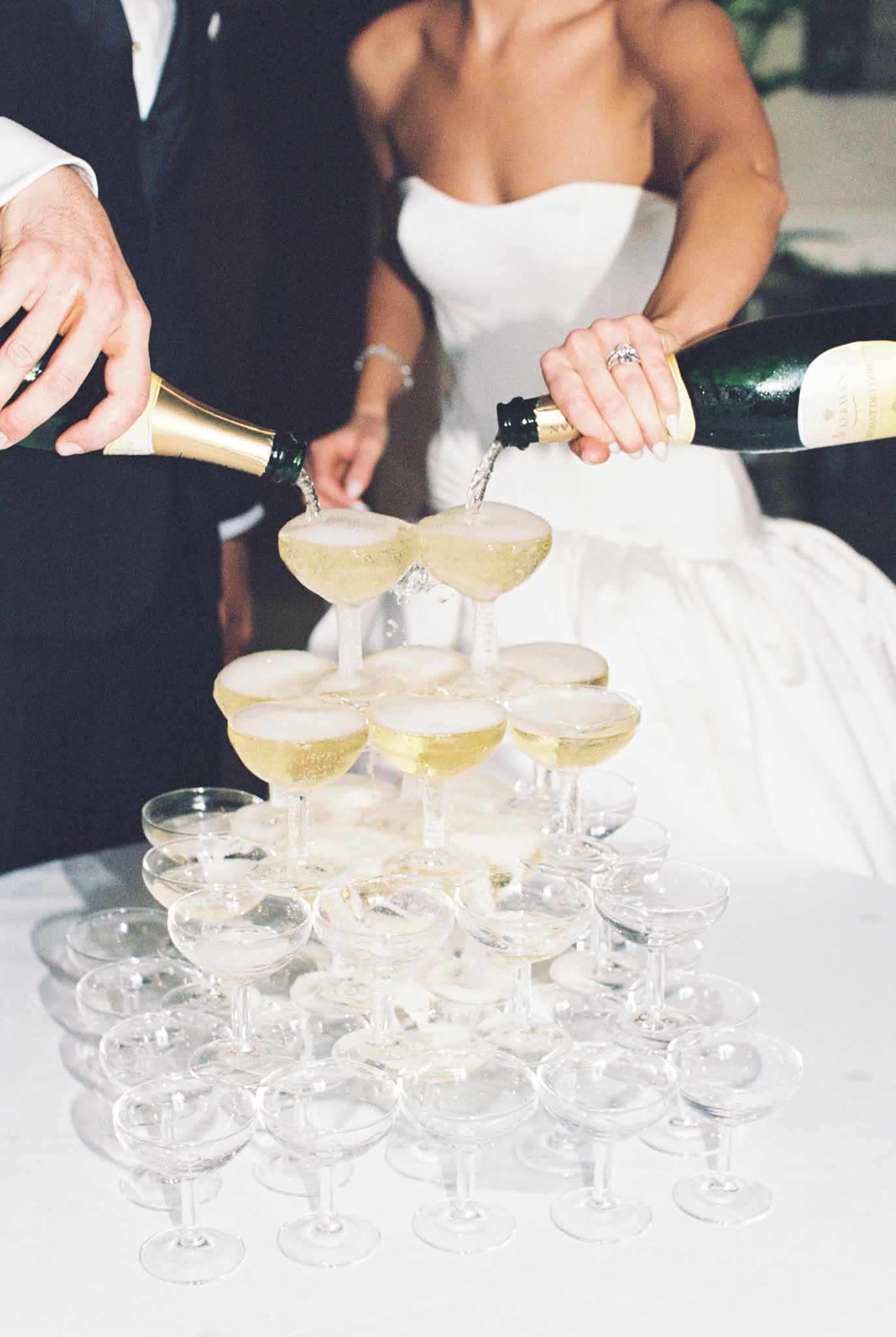 Bride and groom pouring wine into a champagne glass tower at Château de Jalesnes, close-up shot