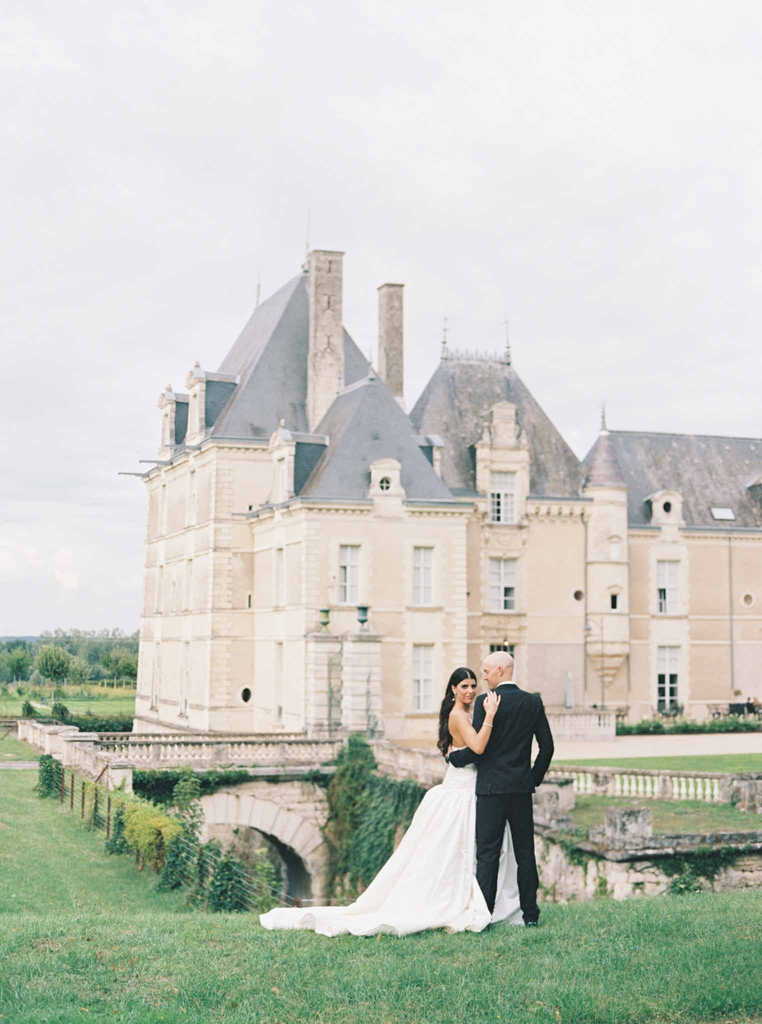 Bride and groom posing on manicured lawn with French Renaissance château in background