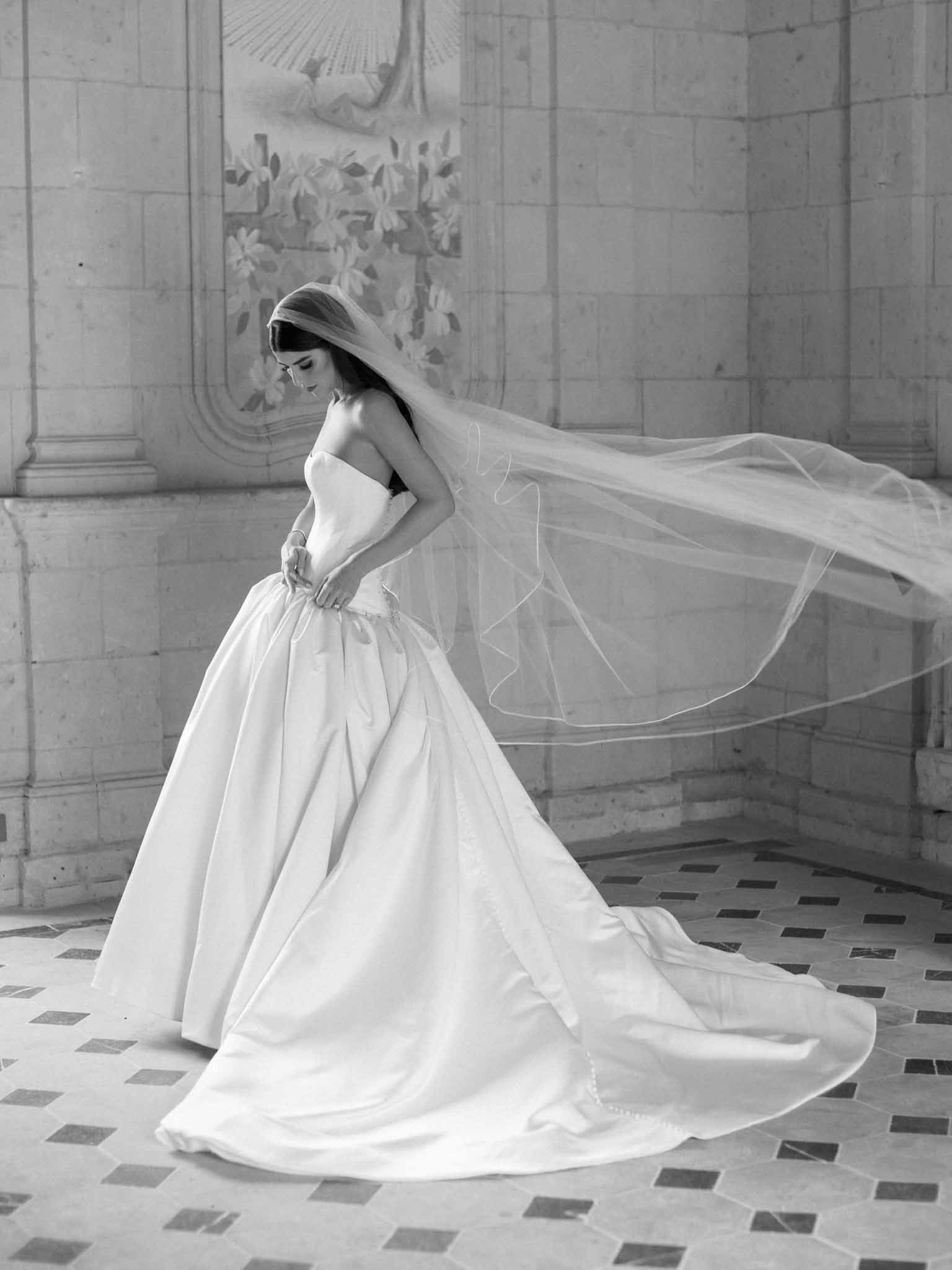 Black and white bridal portrait in profile showing strapless gown and flowing veil in ornate gallery