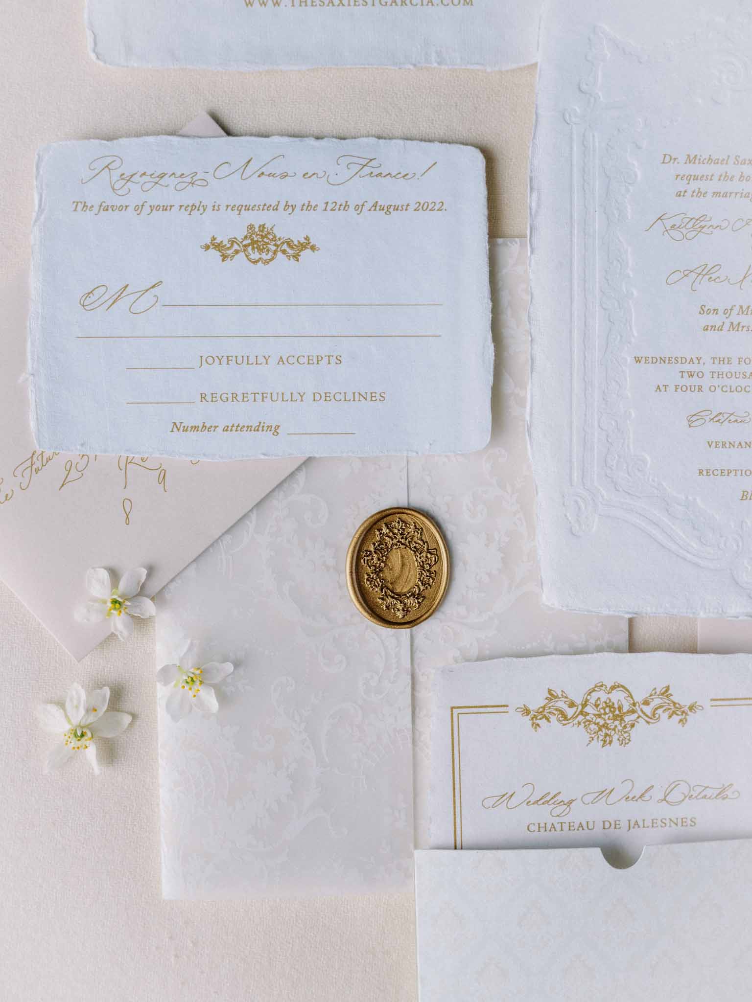 Flat lay of cream and gold wedding stationery suite with gold wax seal, embossed envelopes and small white flowers.