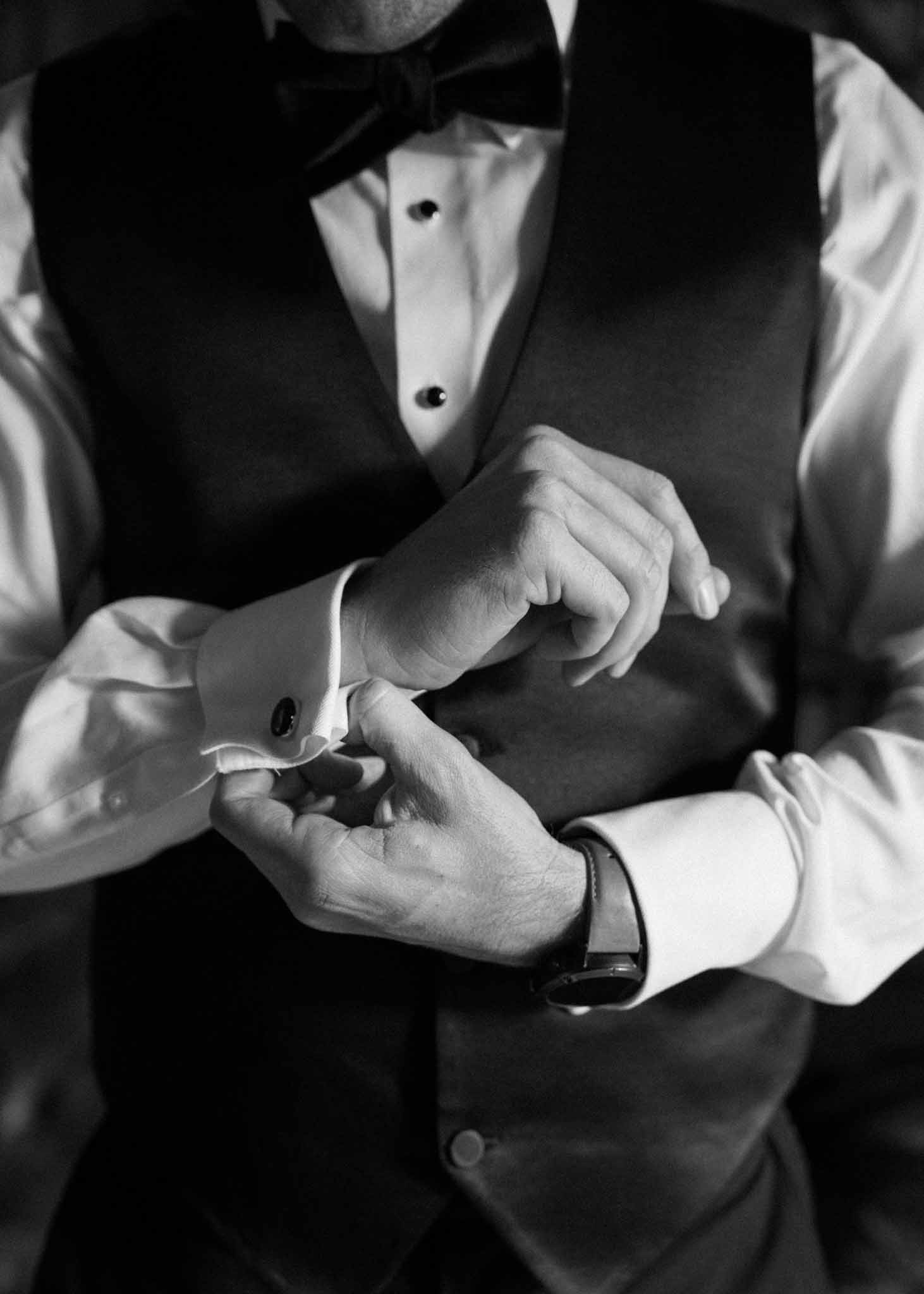 Black and white close-up of groom adjusting cufflinks in formal morning dress with bow tie