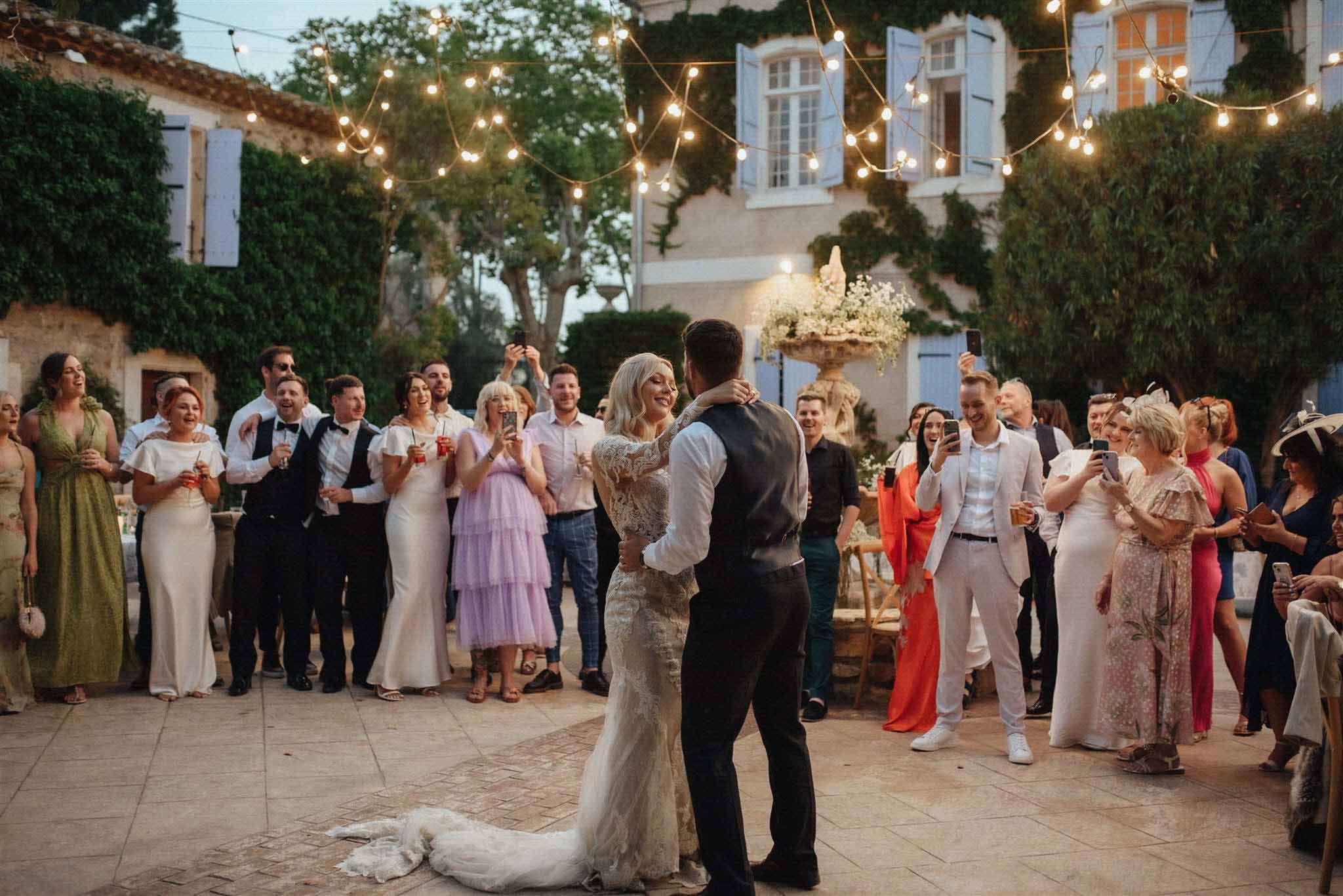 Bride and groom first dance in a Mediterranean courtyard with string lights as guests form a circle around them