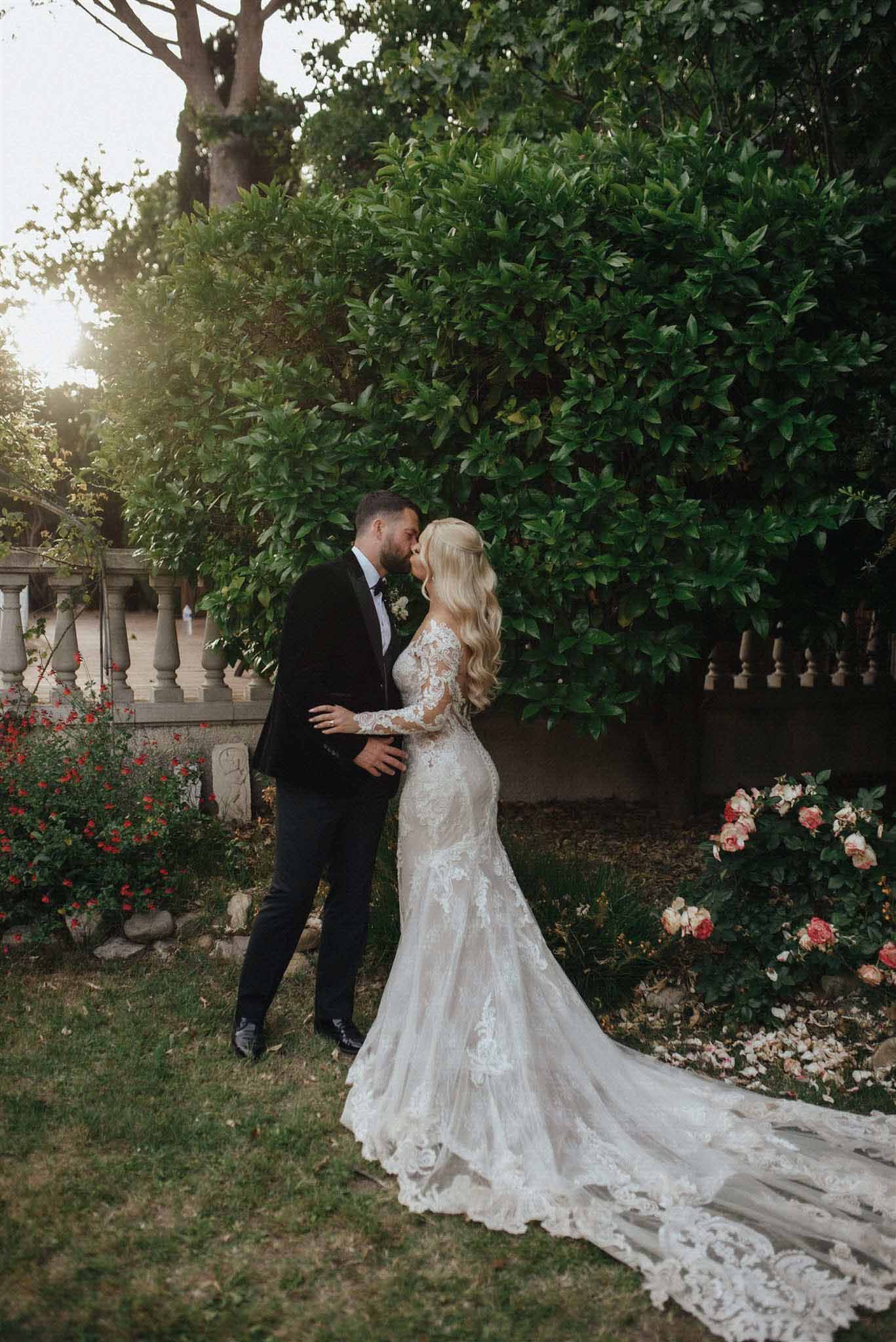 Couple sharing an intimate kiss in a lush garden with stone balustrade, ivy, and blooming red roses