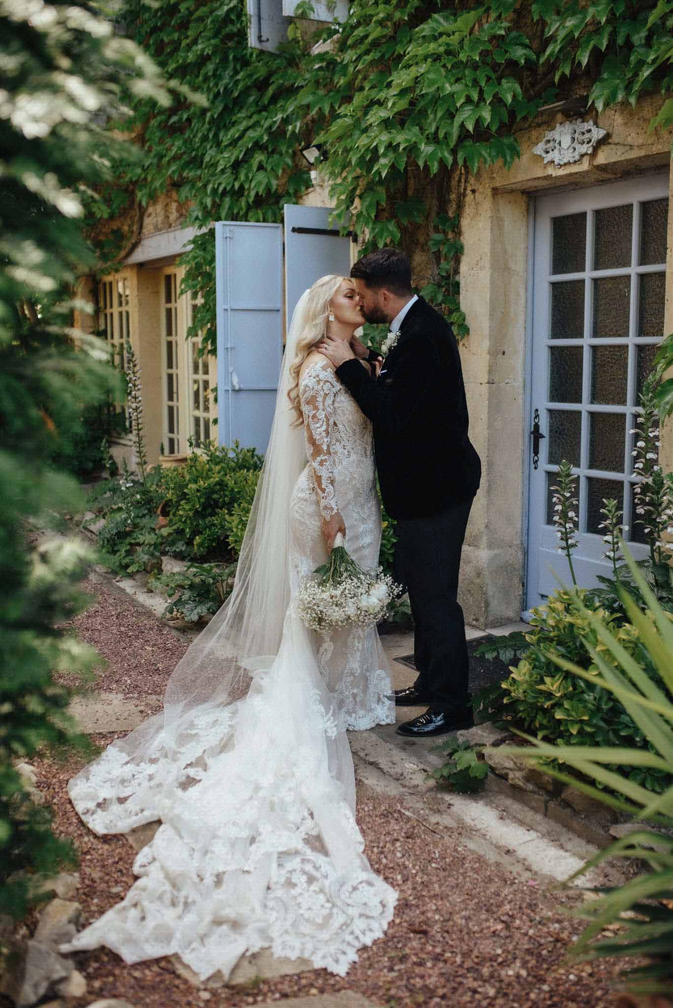 Bride and groom sharing intimate moment in ivy-covered courtyard with blue shutters and baby's breath bouquet