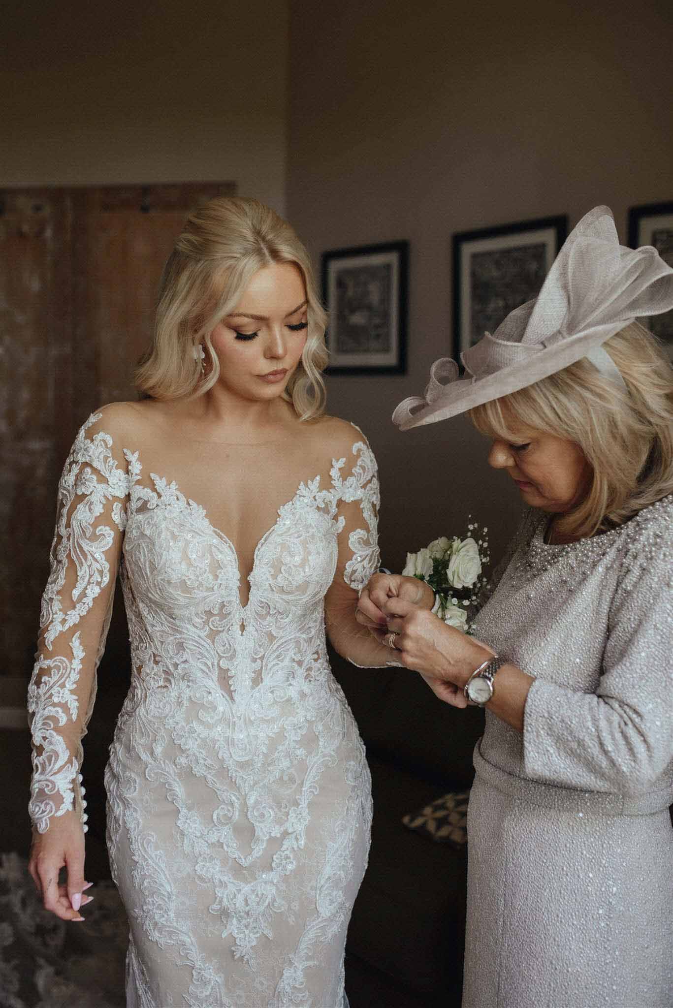 Bride in ivory lace gown with mother pinning white rose corsage during getting ready