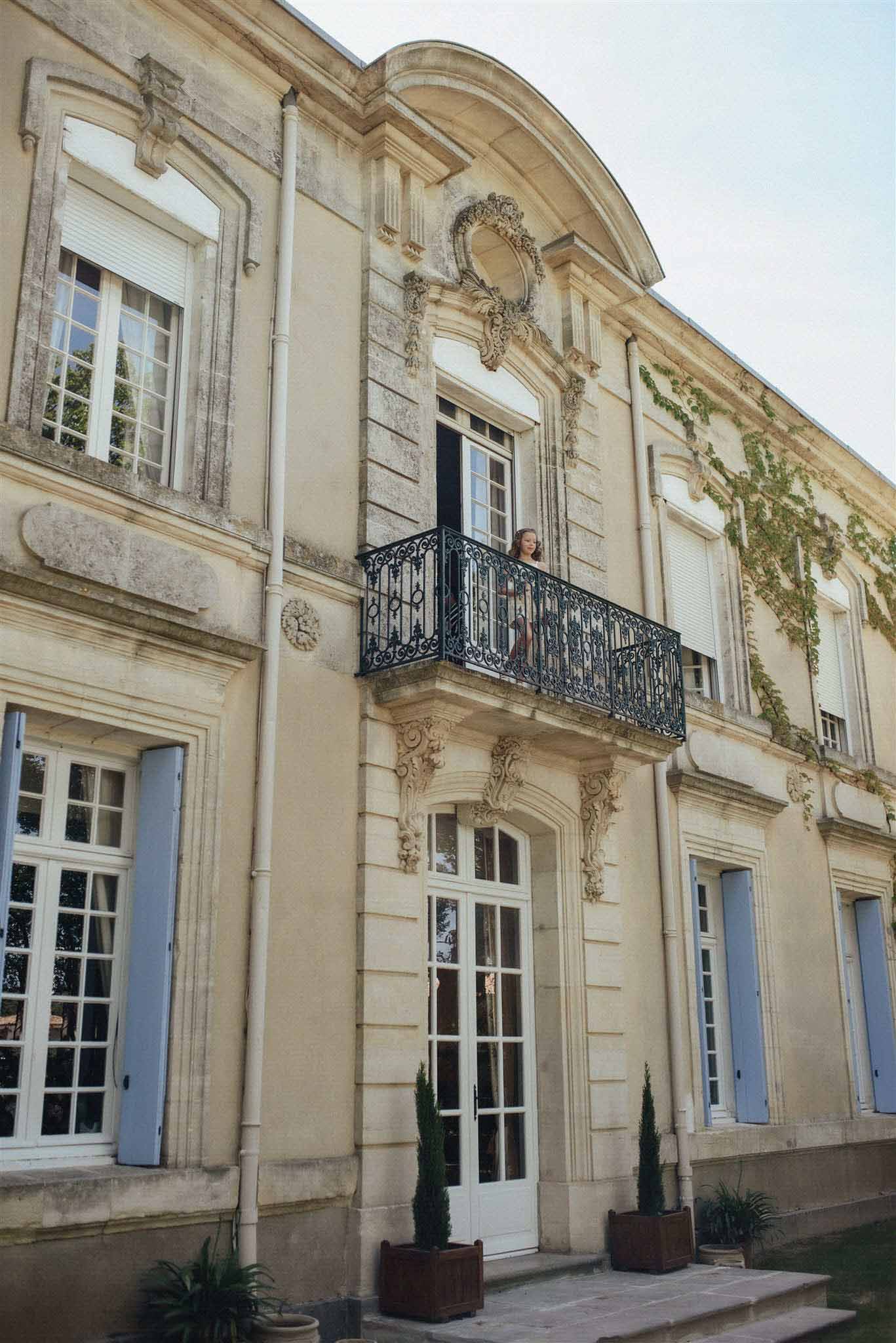 Classical French mansion with cream neoclassical facade, fluted pilasters, mansard roof and figure on Juliet balcony