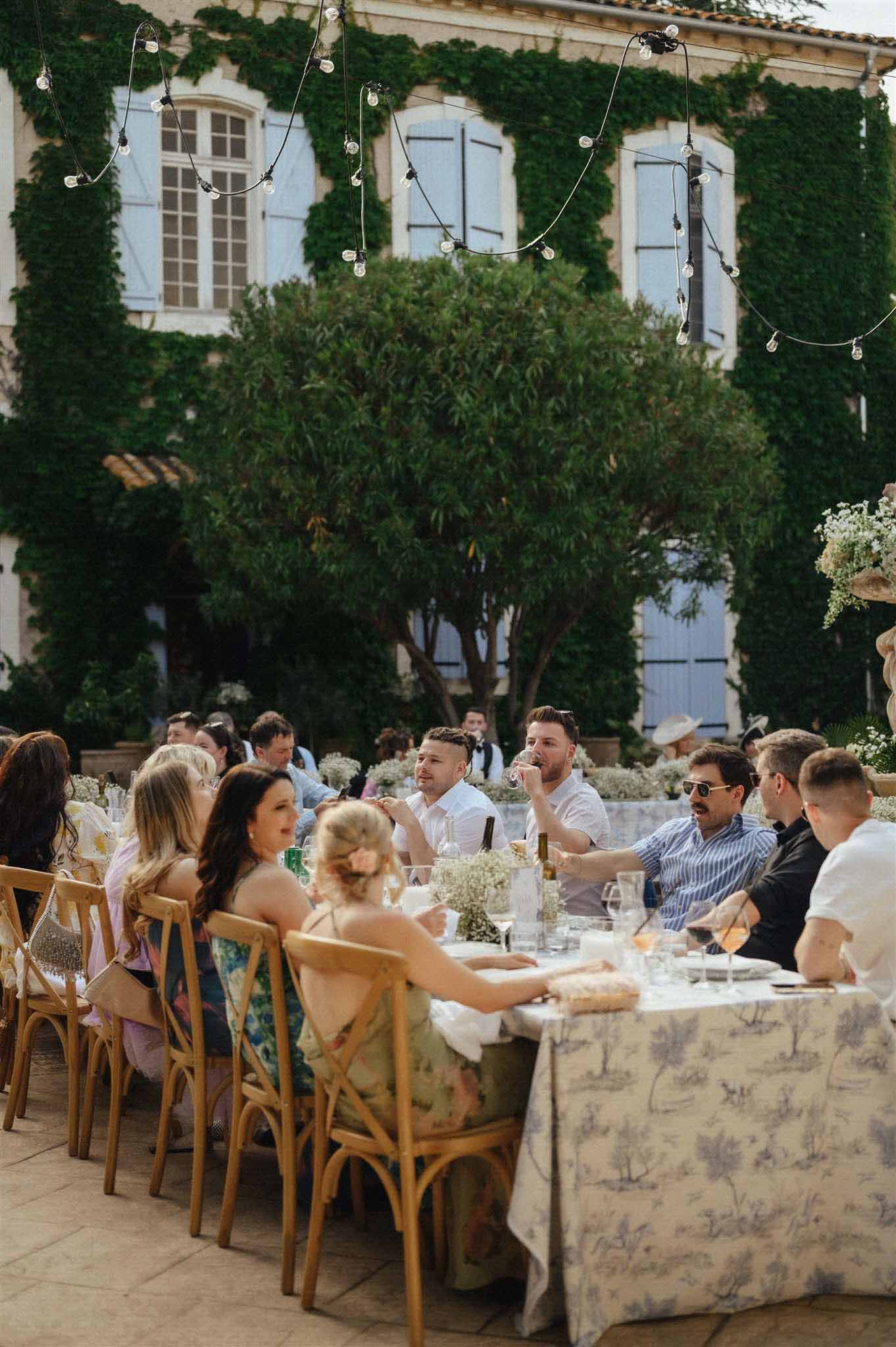 Guests dining in ivy-covered courtyard with pendant lights and baby's breath centerpieces