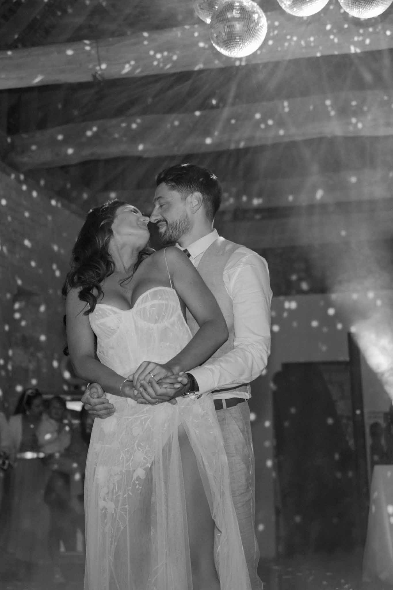 Black and white photo of couple embracing during first dance with disco balls and string lights