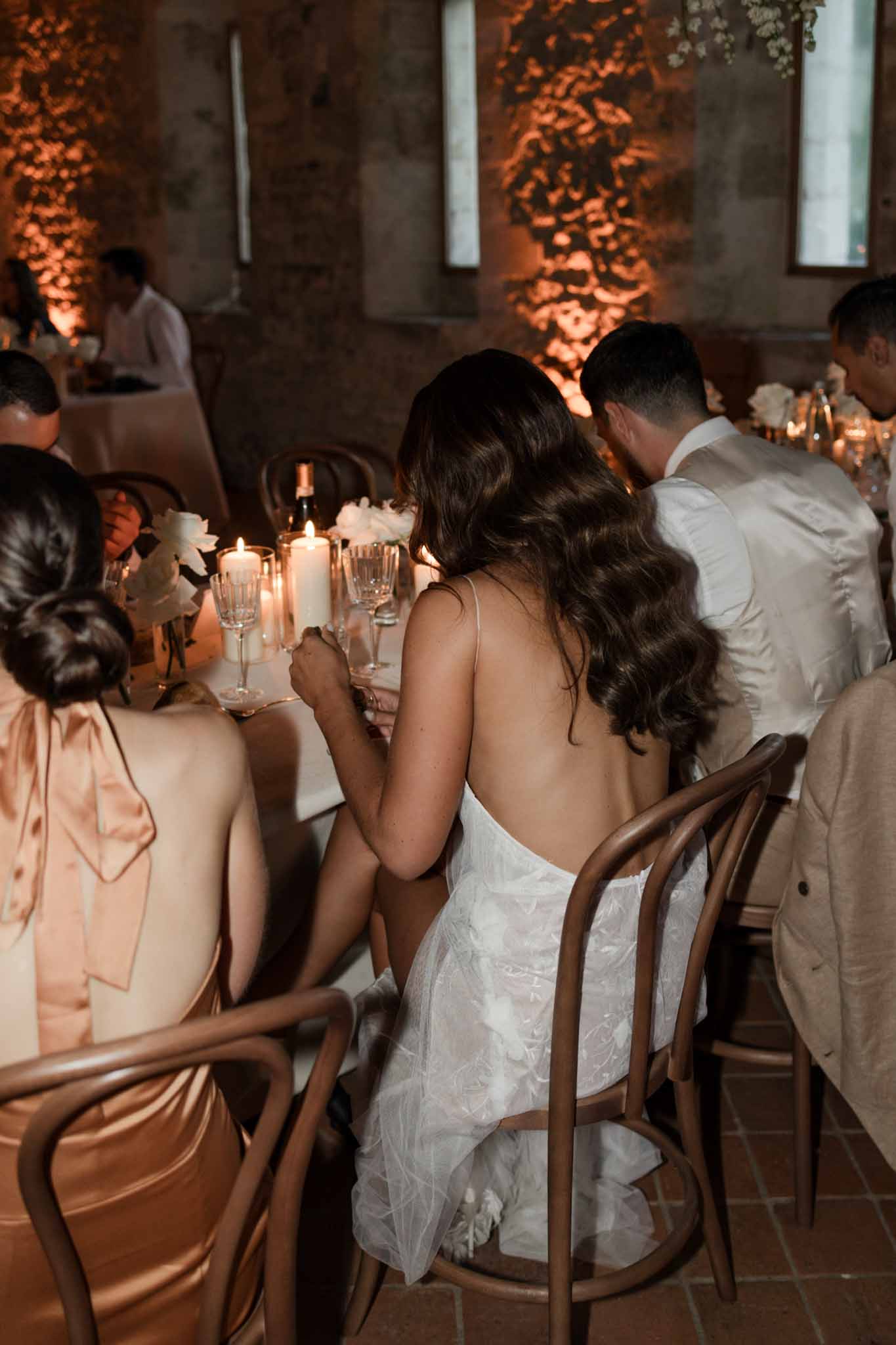 Bride in open-back lace dress at industrial concrete venue dinner with orange uplight and ivy shadow projections