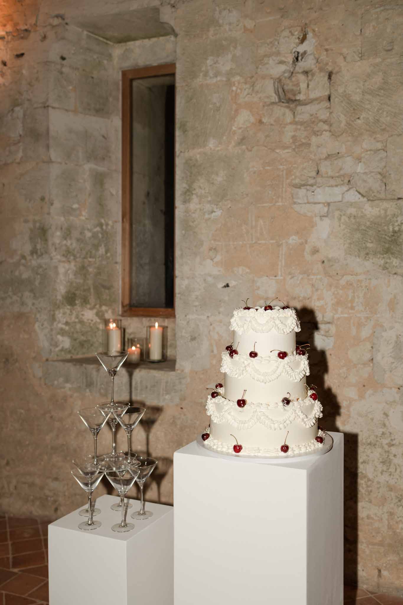 Three-tier white wedding cake with red cherry decoration and champagne tower at Abbaye Noce Machine