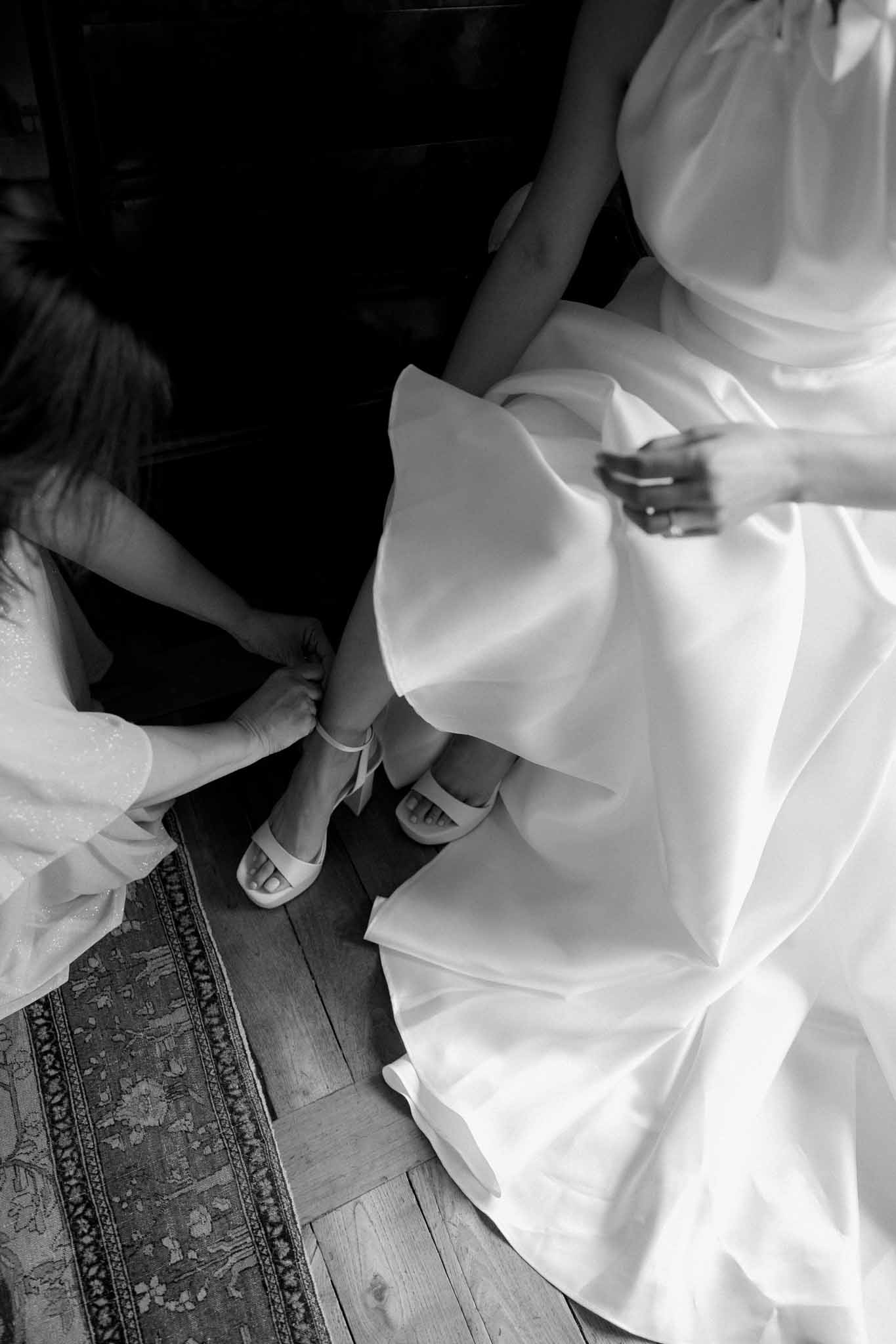 Bride putting on wedding shoes while getting ready at Château de Bouthonvilliers, black and white