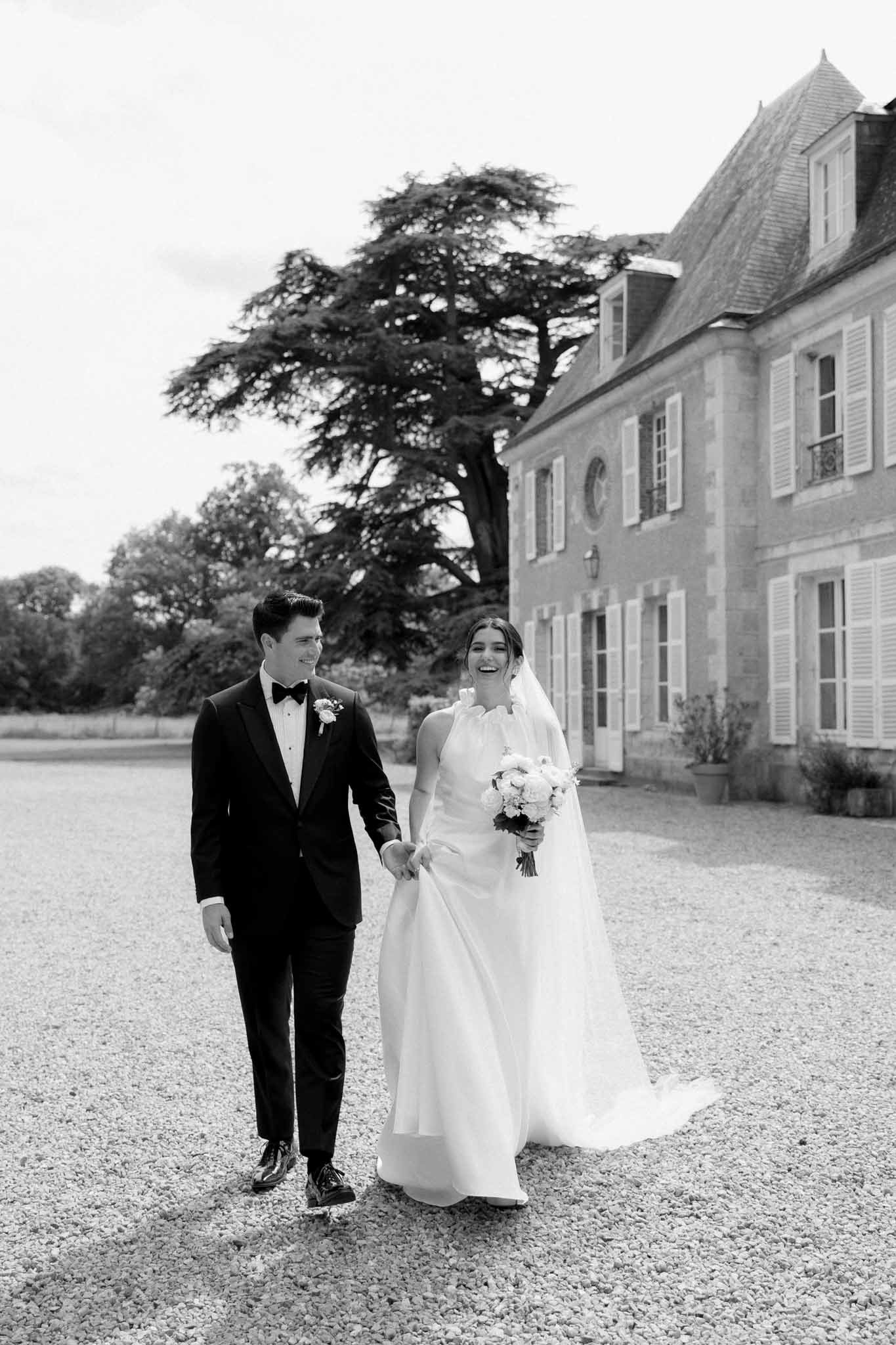 Black and white photo of bride and groom holding hands walking at Chateau de Bouthonvilliers by F Mary