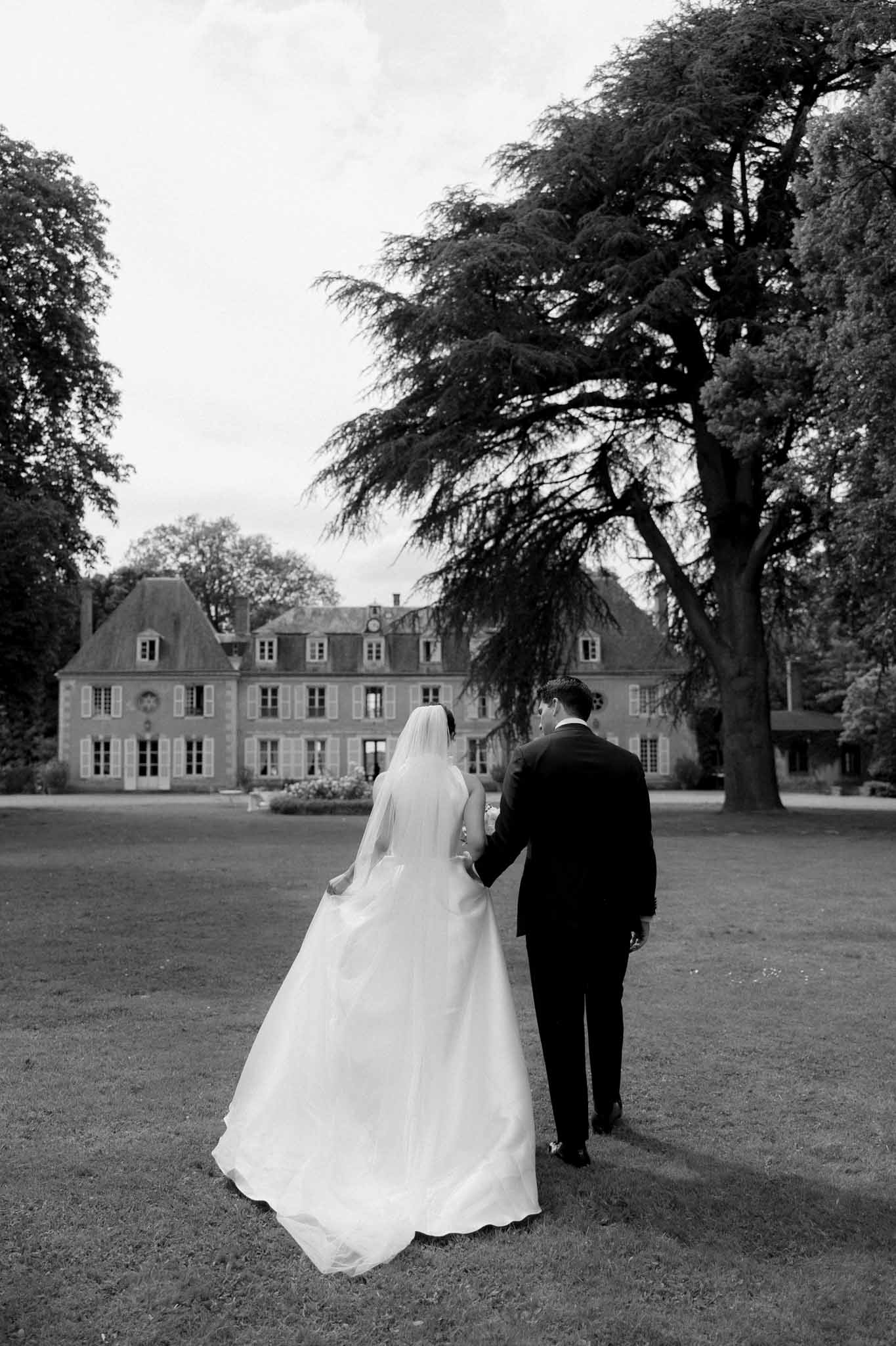 Bride and groom walking away from camera at Château de Bouthonvilliers, black and white photograph