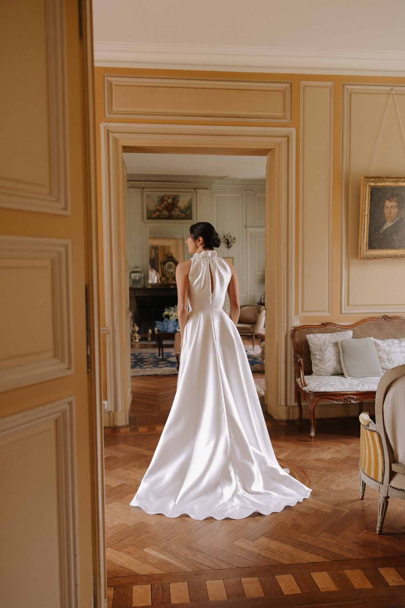 Bride photographed from behind in ivory silk halter gown with long train in classical chateau interior with paneled walls