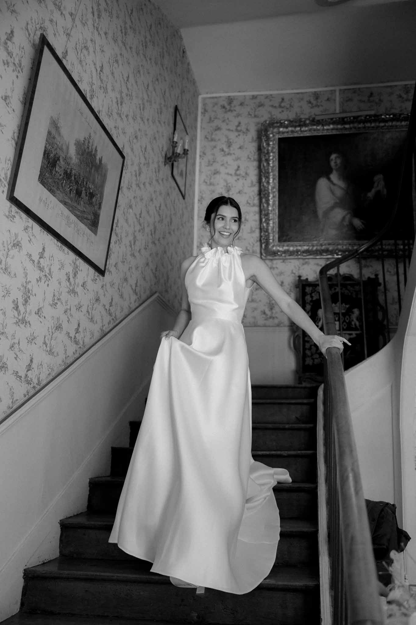 Black and white portrait of bride descending staircase in historic hallway with vintage wallpaper