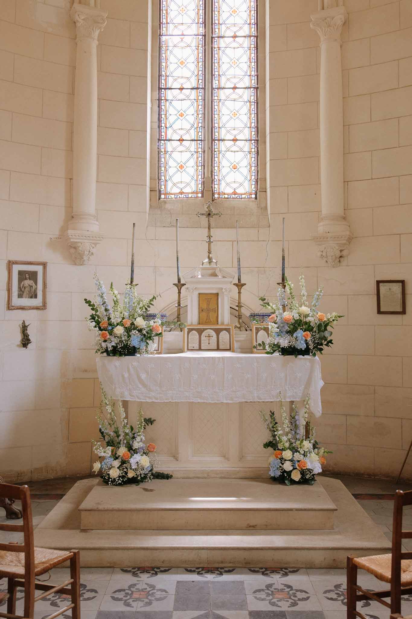 Chapel altar with floral arrangements in cream, blue, and coral tones beneath stained glass window