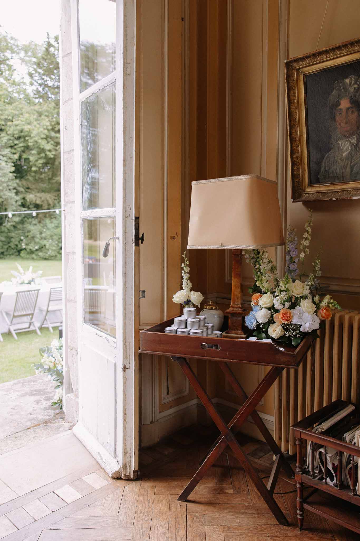 Classical room with cream linen lamp, apricot rose and blue hydrangea arrangement, wooden paneling and garden view