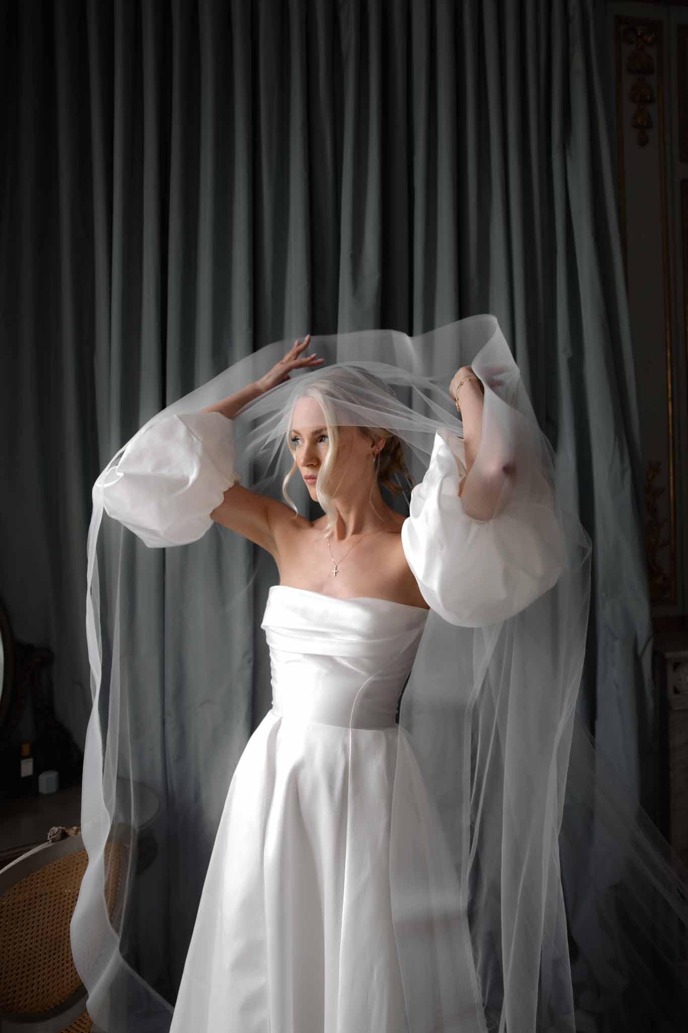 Bride arranging her tulle veil with both hands against charcoal curtain backdrop