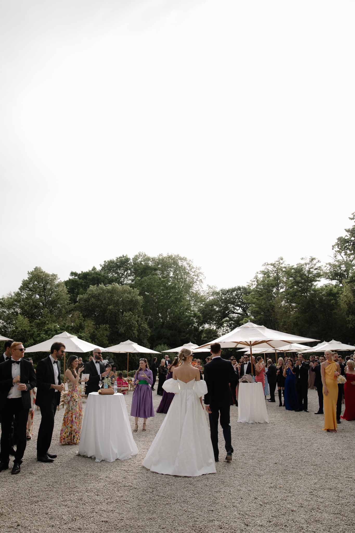 Cocktail hour in open-air garden with white marquee tents and guests in black tie and jewel-tone dresses