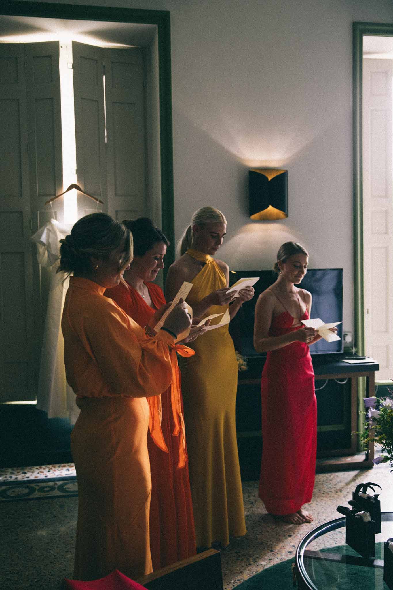 Four women in jewel-toned gowns reading speeches during reception in contemporary interior