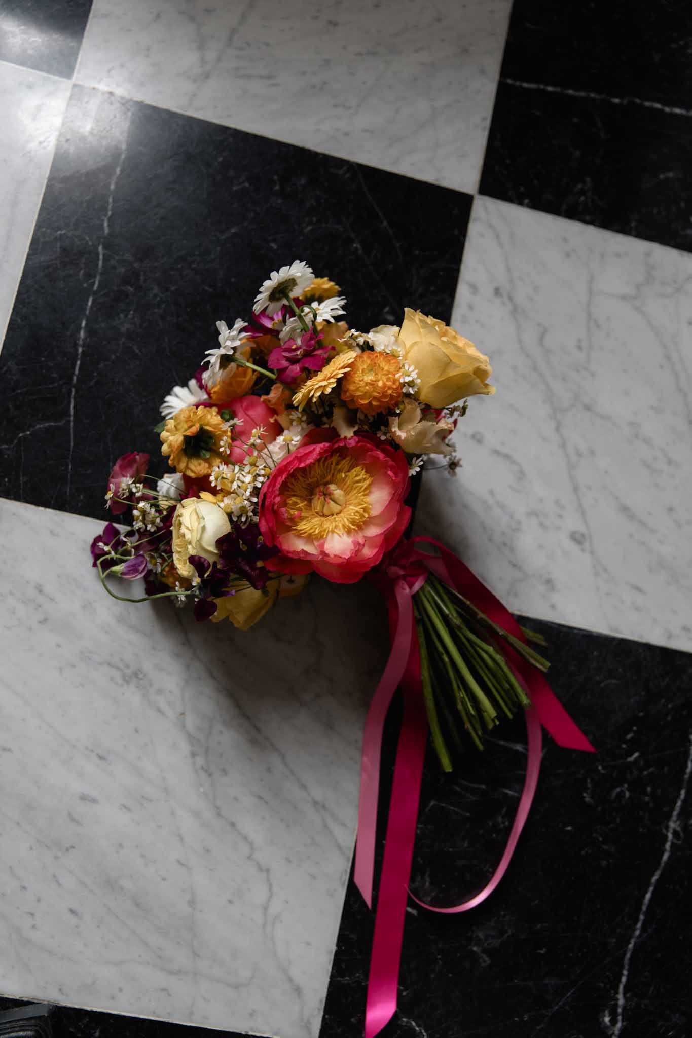 Vibrant bridal bouquet of fuchsia peonies, golden daisies, and cream roses on marble floor