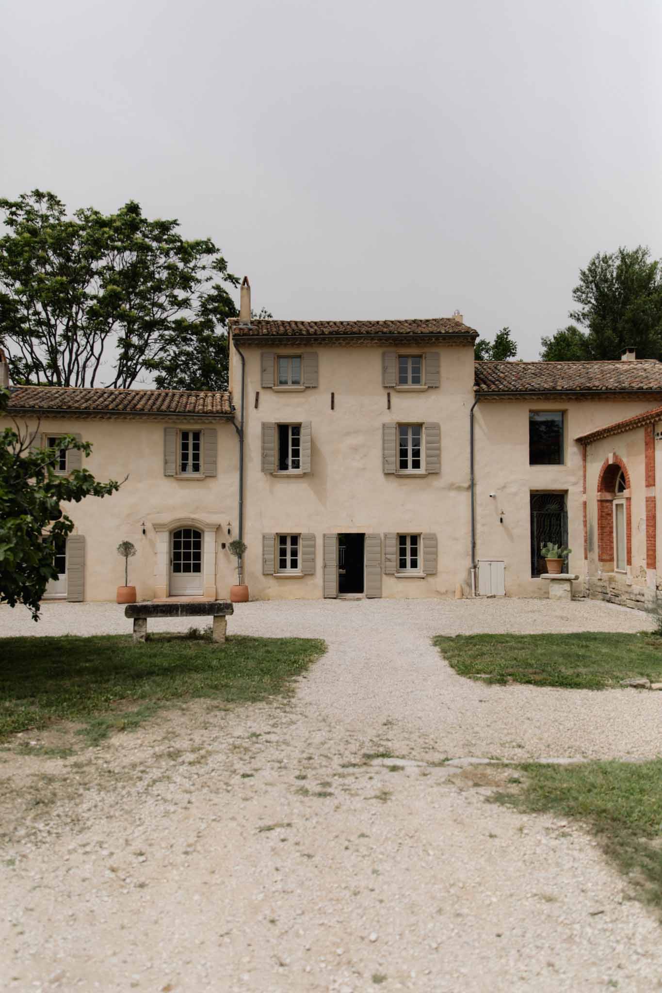 Traditional Tuscan villa with cream render and terracotta roof tiles, stone bench, and mature framing trees