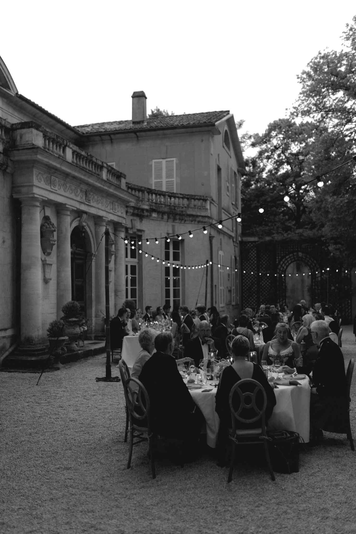 Elevated view of wedding reception dinner in classical courtyard with guests at long tables under string lights