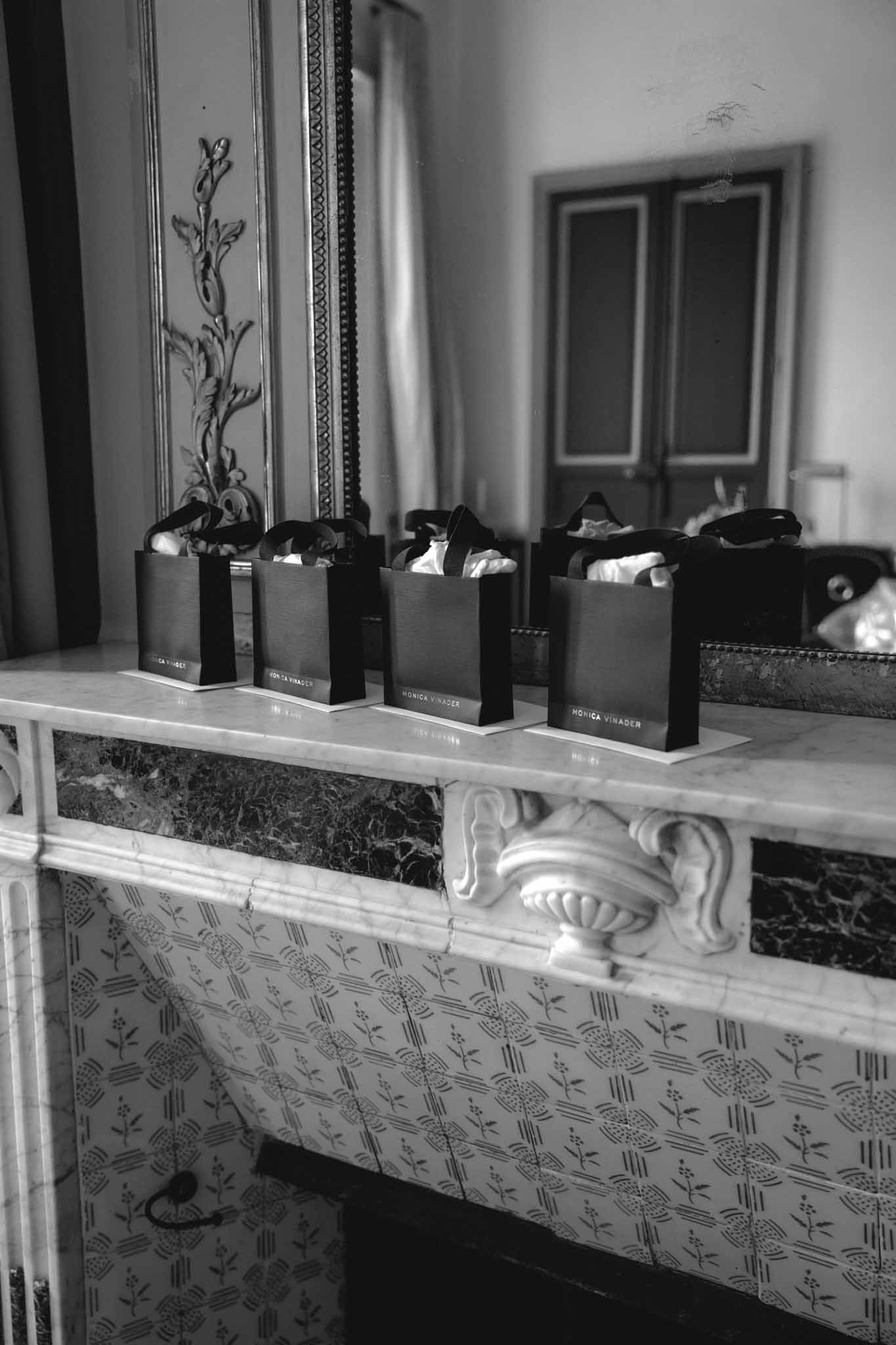 Black paper gift bags with white tissue paper arranged on ornate classical mantelpiece with carved molding and botanical wallpaper