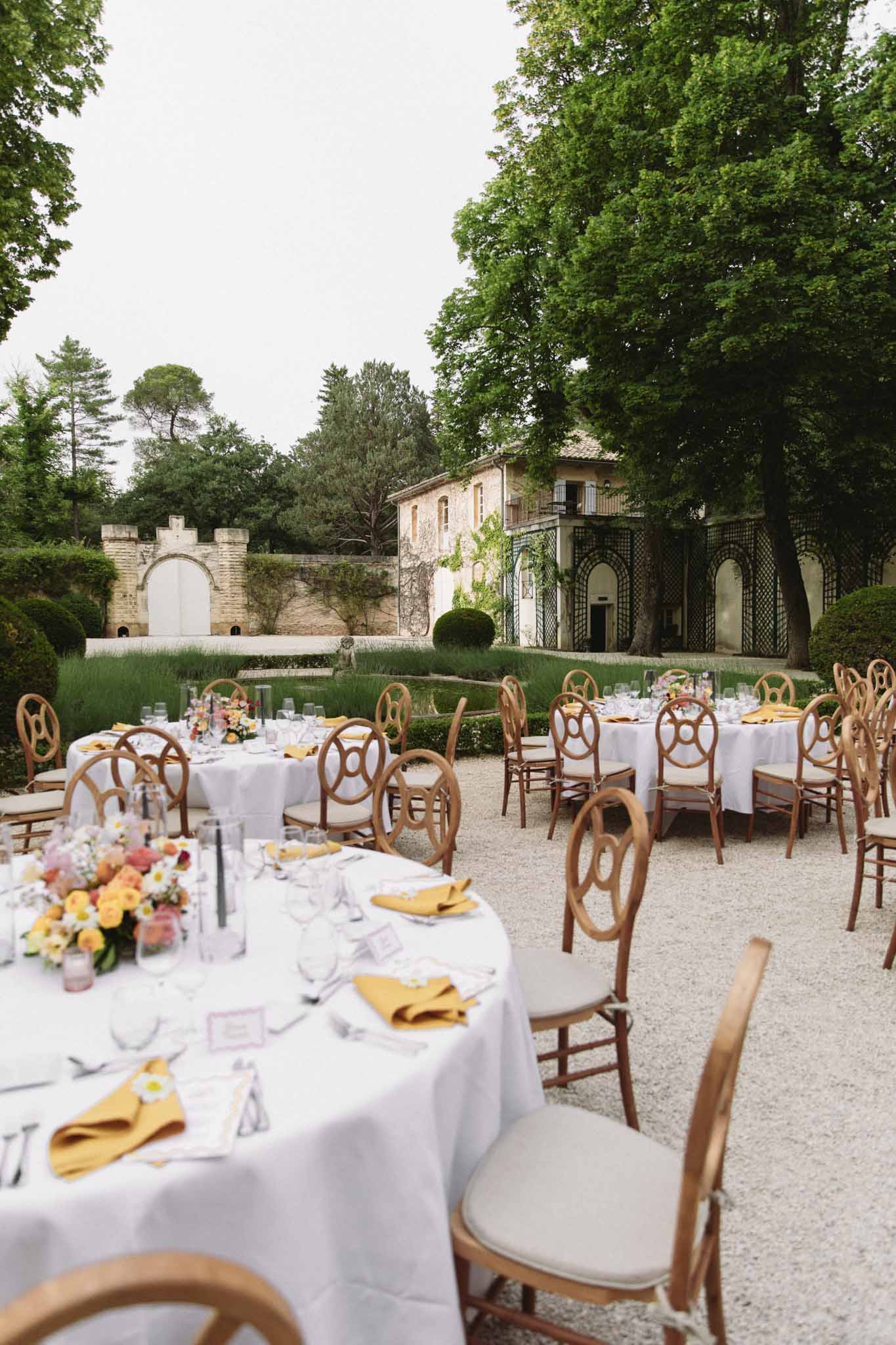 Outdoor reception with round tables on gravel courtyard of Tuscan-style villa with terracotta roof and ivy archway