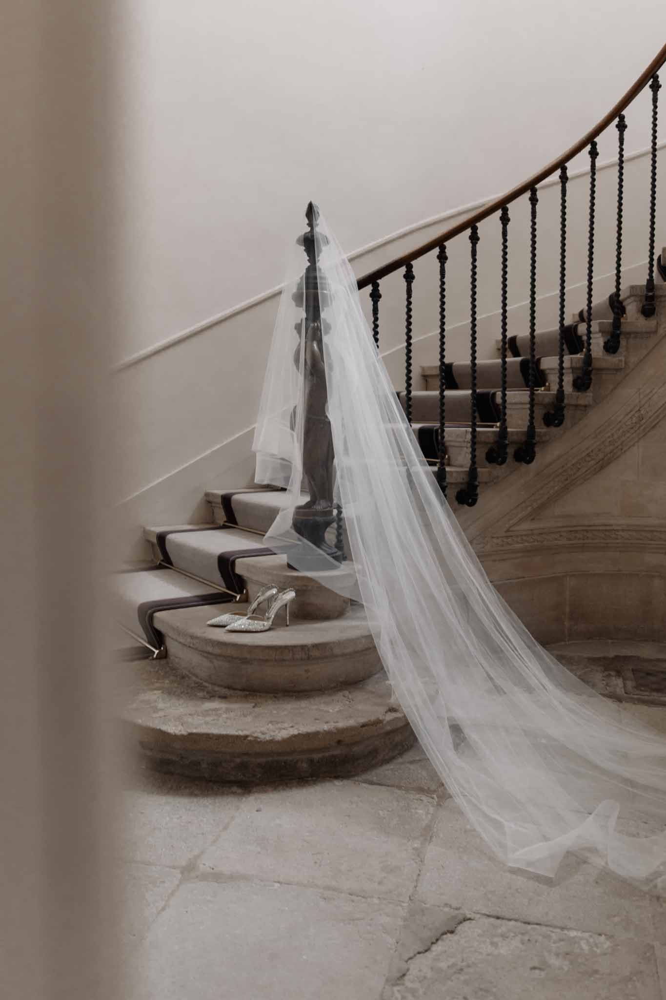 Bride in ivory dress sits on stone staircase, her long veil cascading dramatically down the steps behind her