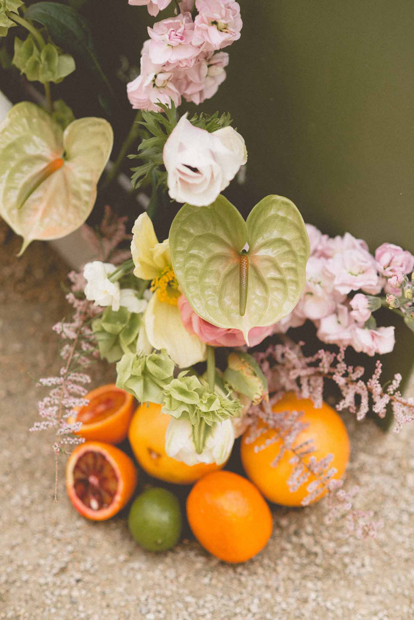 Floral arrangement with cream anthuriums, blush stock, and yellow hellebores styled with halved blood oranges