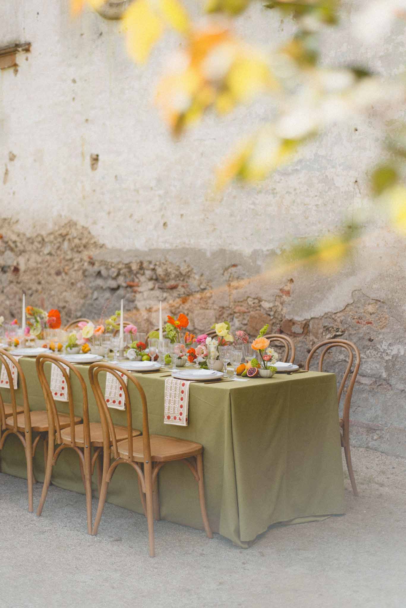 Olive linen table with orange poppies hot pink ranunculus blood orange slices and bentwood chairs
