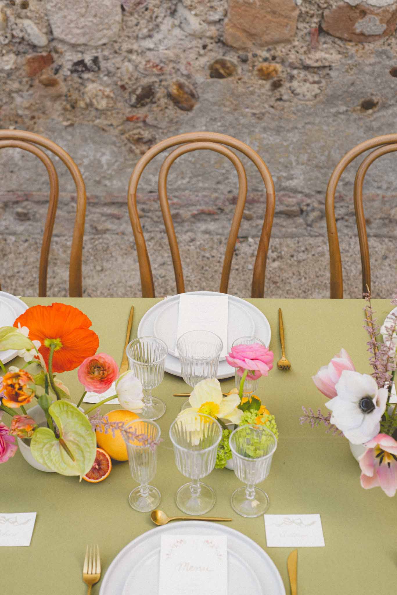Reception tablescape with orange poppies, pink ranunculus, blood oranges, olive linen, and bentwood chairs