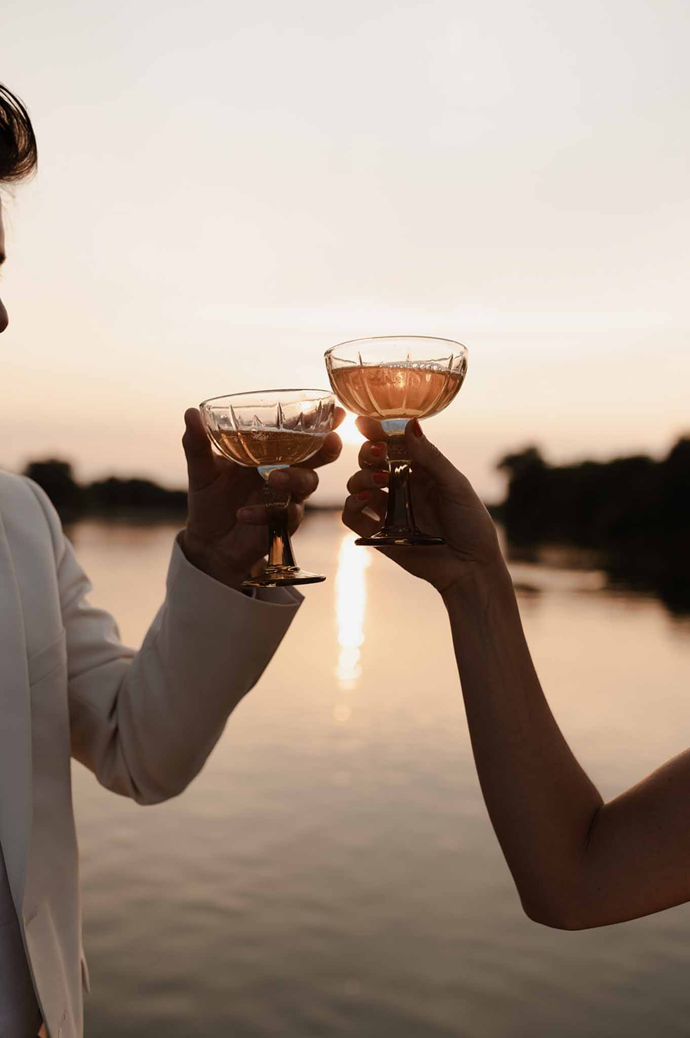 Bride and groom tossing wine glasses by the river at sunset in Loire Valley photographed by Il Keys