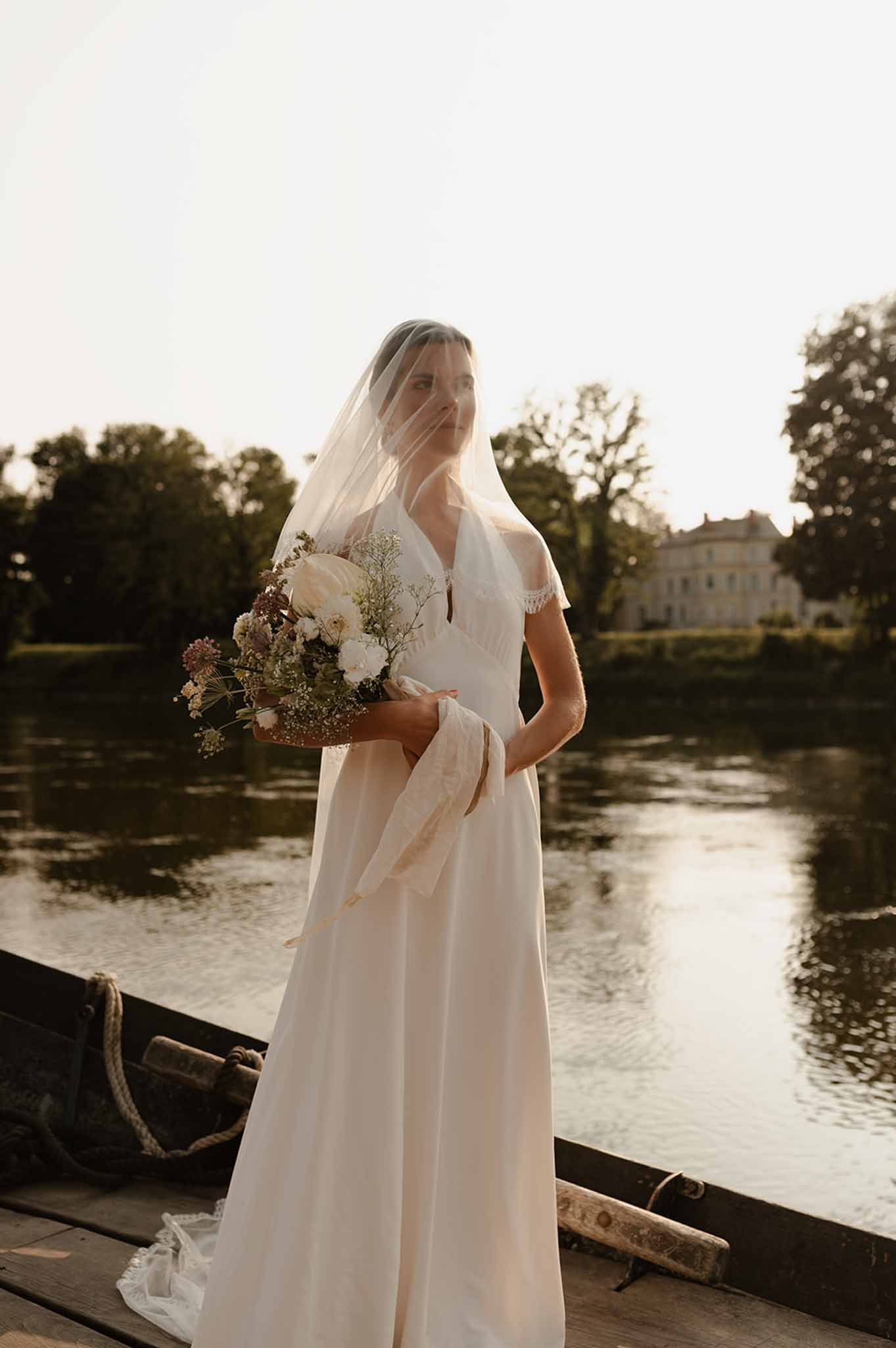 Bride in old Hollywood gown and veil with wind in her hair beside river in Loire Valley photographed by Il Keys
