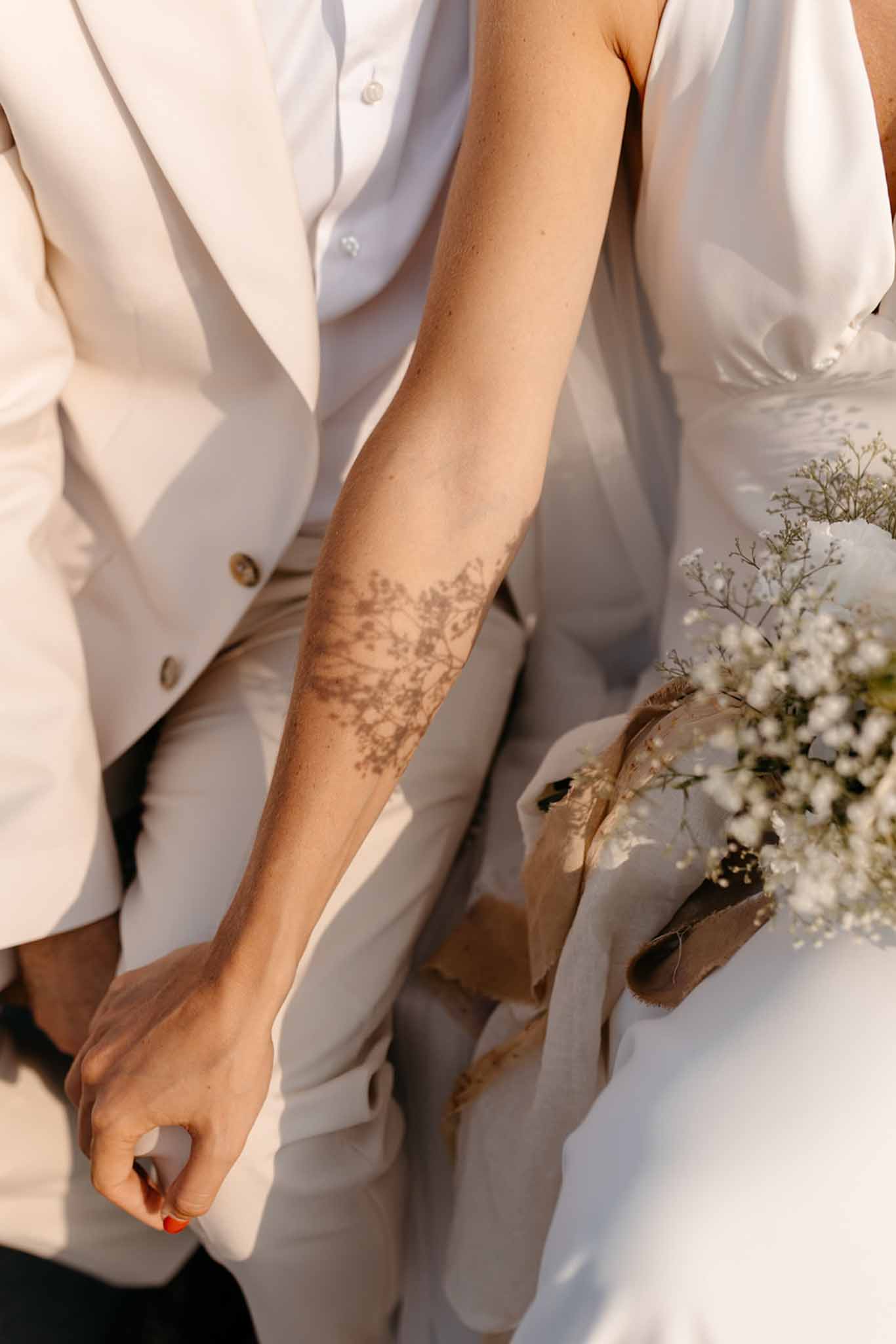 Close-up of couple in matching cream suits holding baby's breath bouquet with henna tattoo