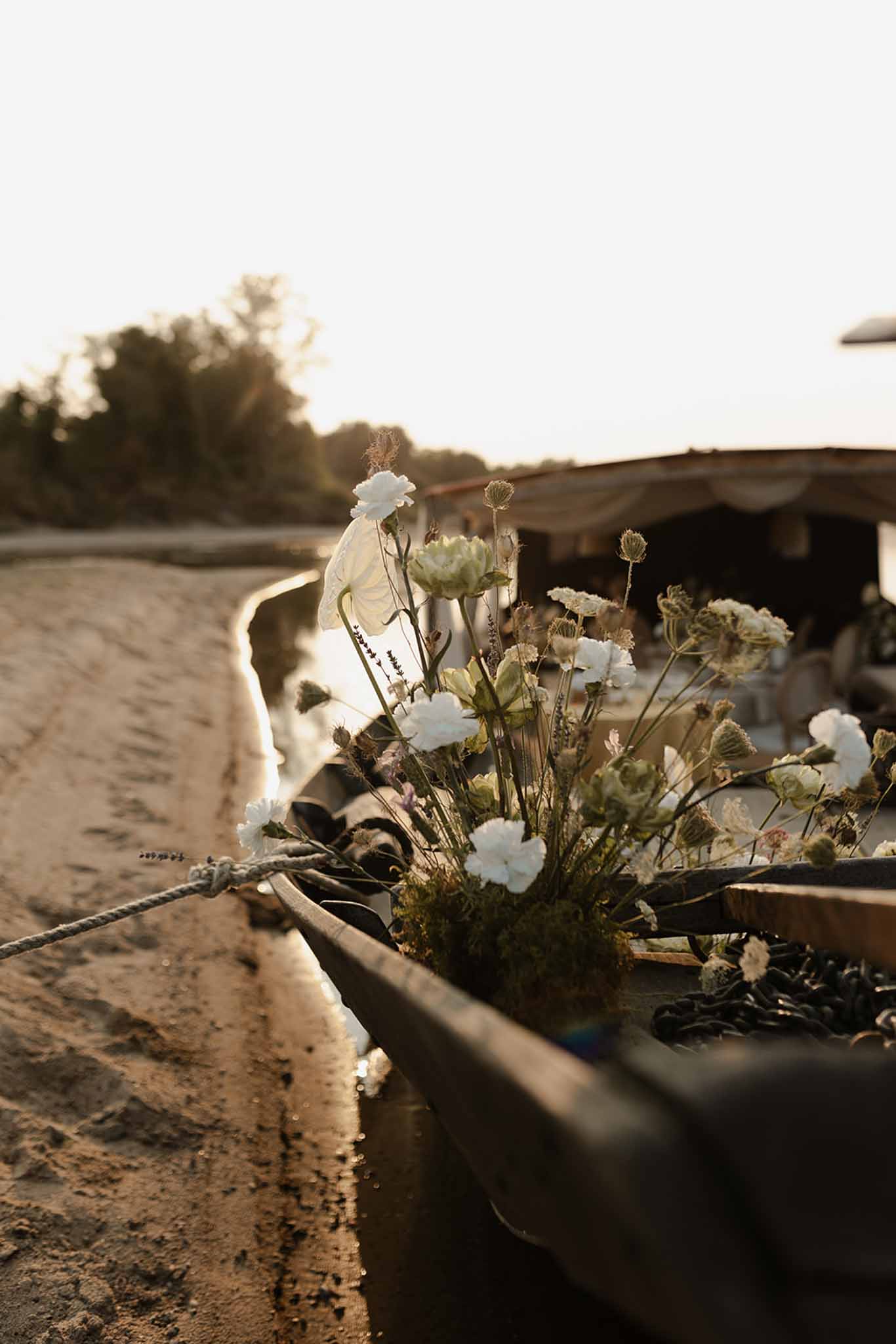 Rustic floral arrangement of ivory carnations tied to weathered wooden rail at golden hour