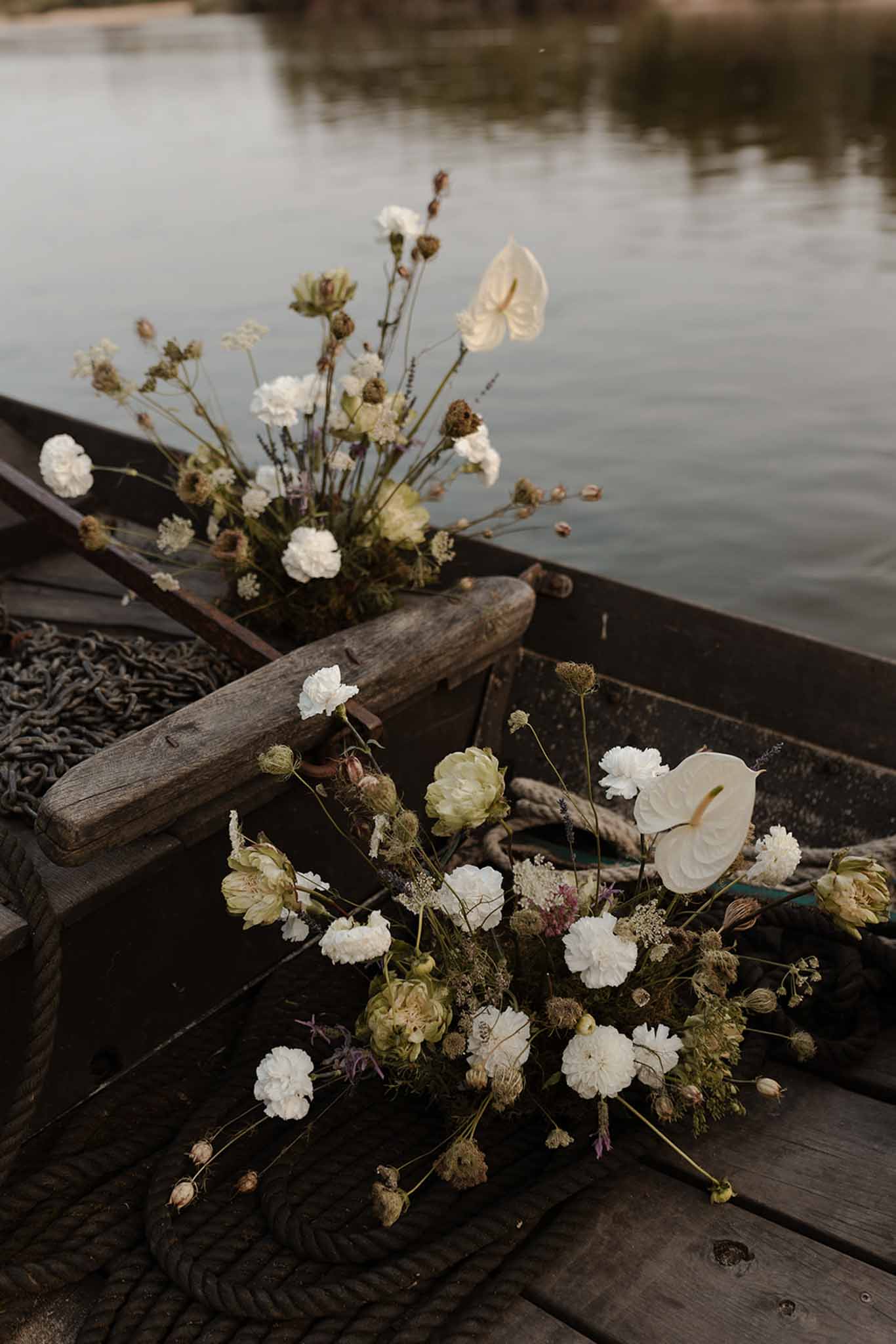 White floral arrangements in a wooden boat at a ceremony venue