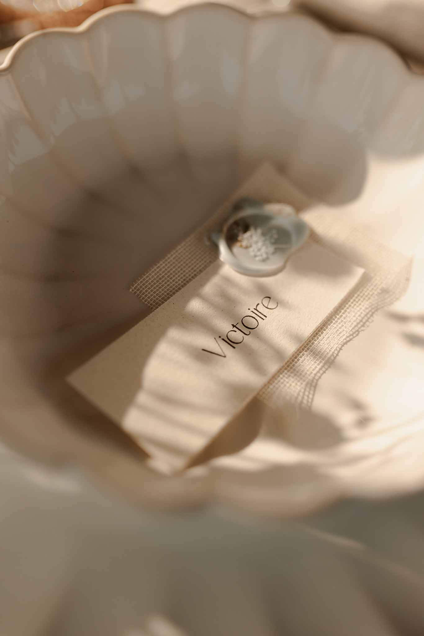 Diamond engagement ring resting on ivory escort card labeled Victoire tied with neutral ribbon on pleated linen