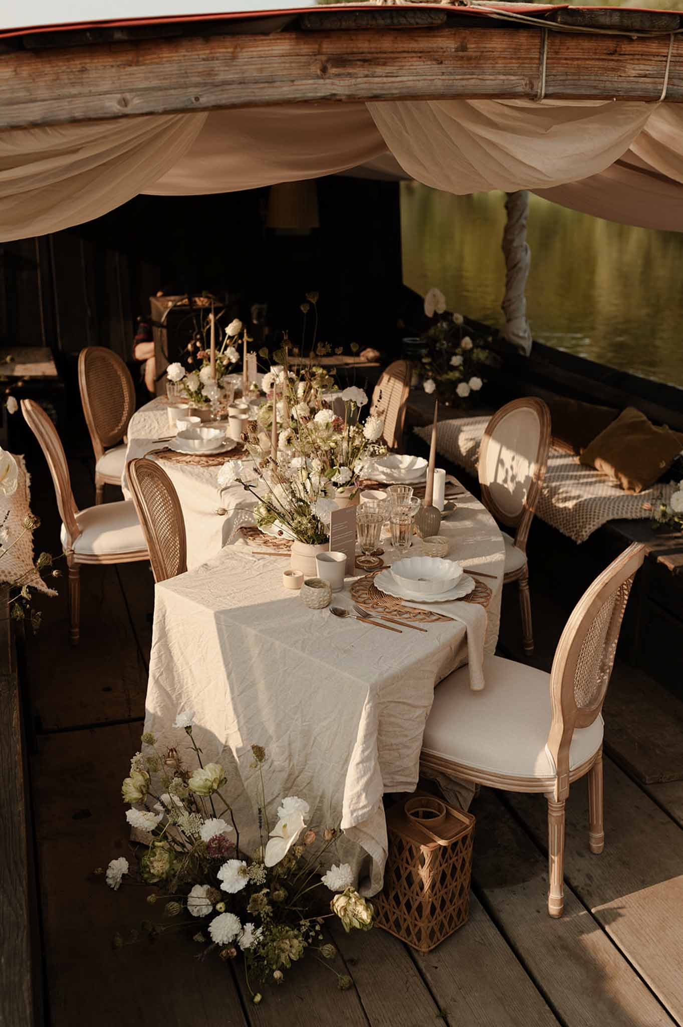 Reception setup in boat venue with cream linen tables, white carnation centerpieces, and draped taupe fabric
